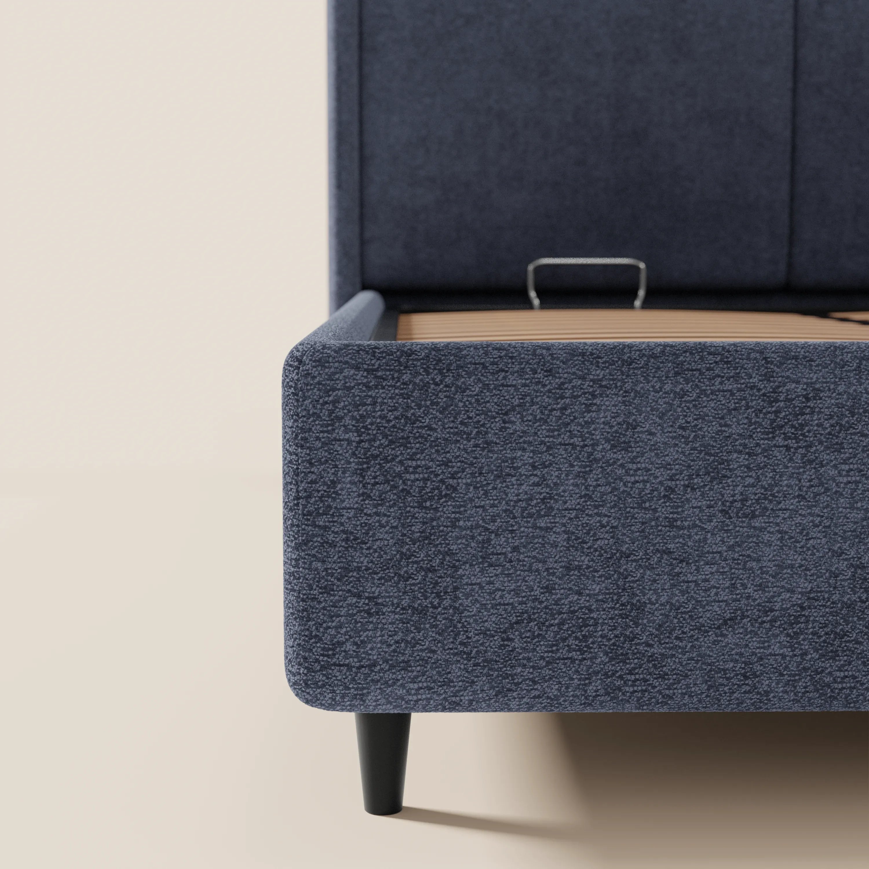 Primo piano del letto di design VALKIRIA di Letti.store, con tessuto blu scuro certificato Oeko-Tex®, angoli arrotondati, gambe affusolate nere, base a doghe in legno e testiera avvolgente con 2 cuscini: lo stile contemporaneo risalta sullo sfondo chiaro.