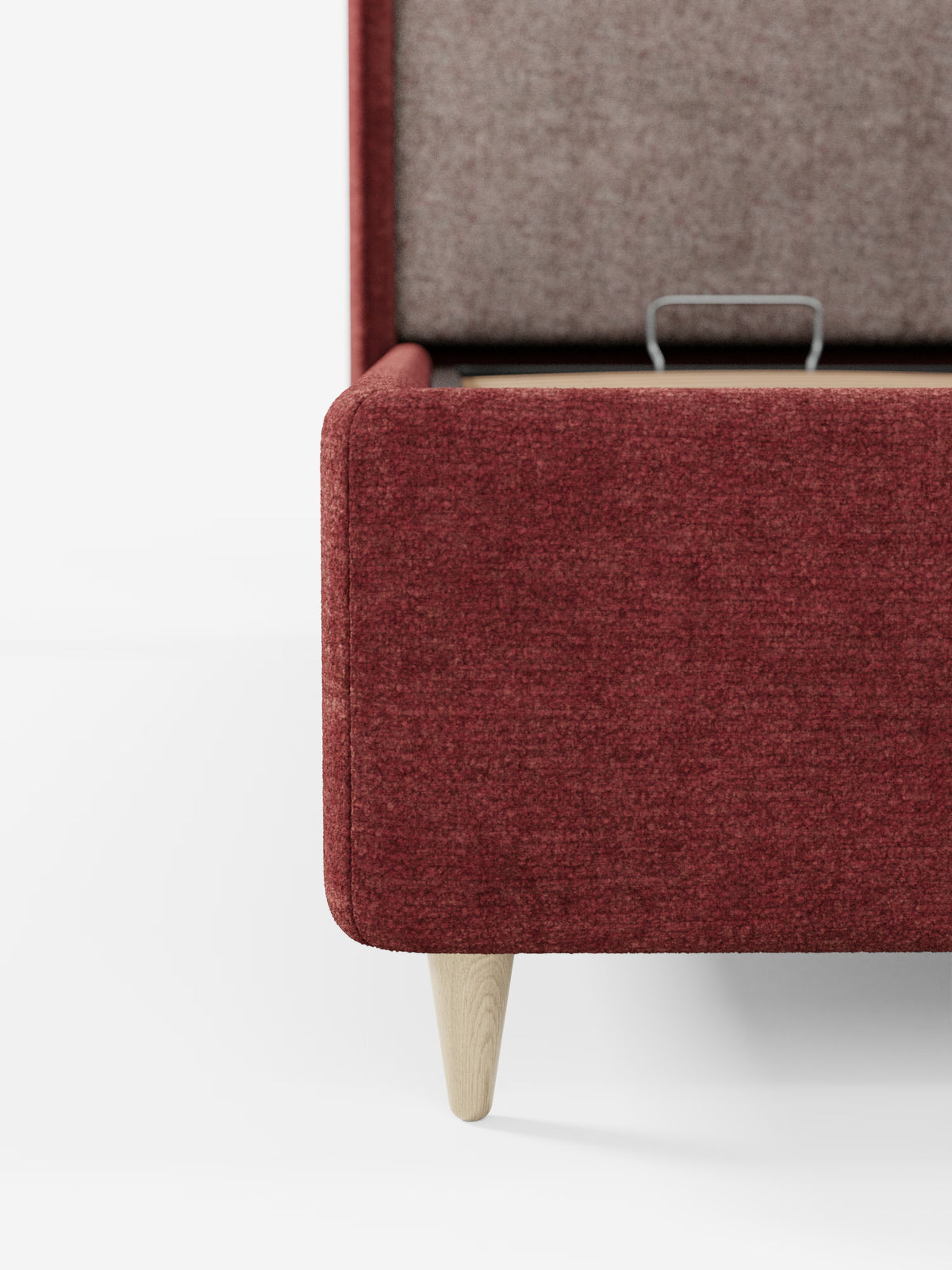 Primo piano di un pouf imbottito rosso con coperchio incernierato parzialmente aperto che rivela il vano contenitore interno: un abbinamento perfetto per il letto imbottito bicolore con vano contenitore VALKIRIA di Letti.store, caratterizzato da cuscini schienali e da una testiera avvolgente e curva. Il pouf poggia su gambe in legno chiaro su uno sfondo bianco, con solo la metà destra visibile nell’inquadratura.