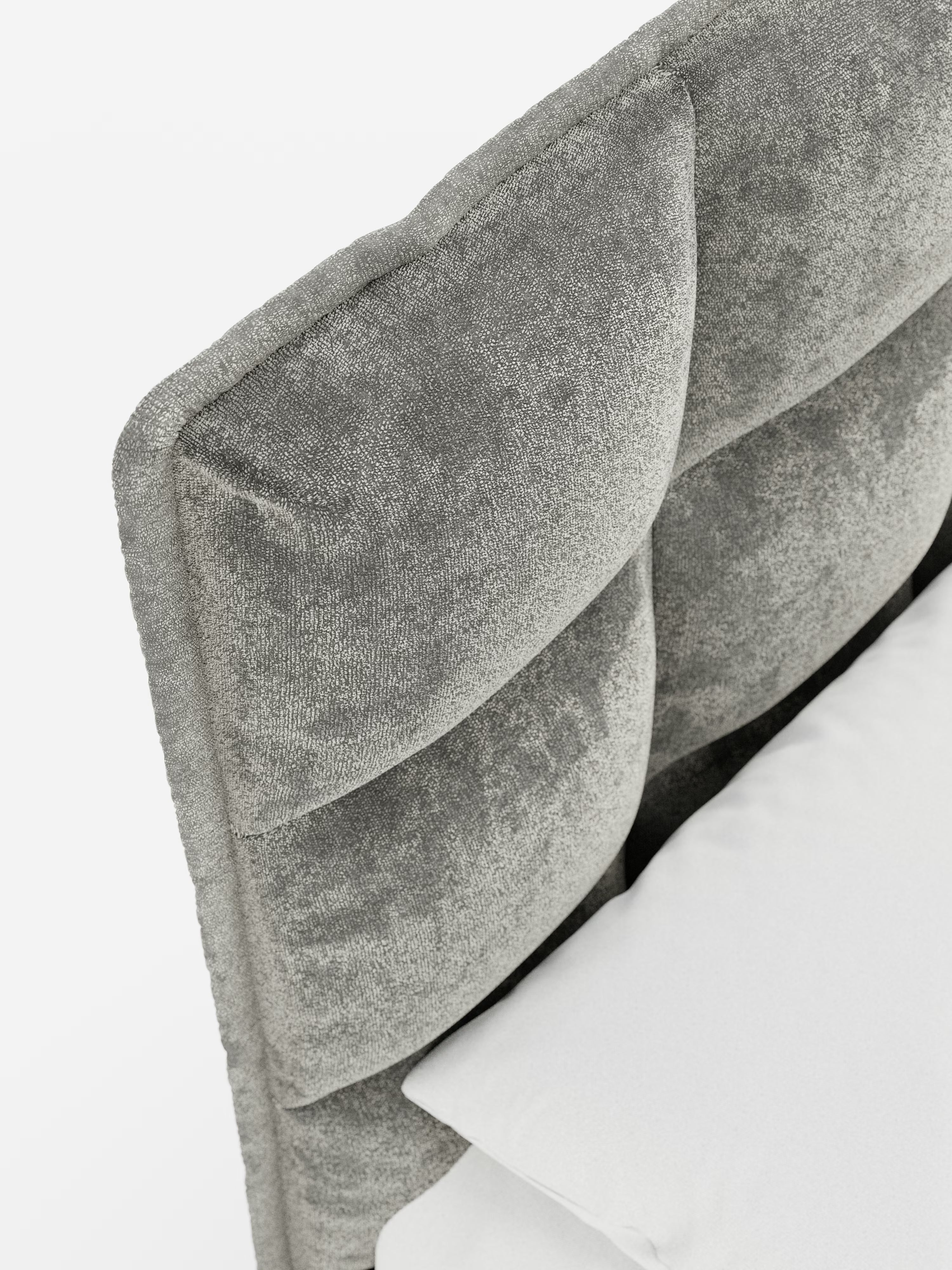 Questo primo piano del letto imbottito AURO con contenitore e testiera capitonné alta in ciniglia Oeko-Tex® di Letti.store mette in risalto la sua testiera in ciniglia grigia, morbida e trapuntata, che evoca l’eleganza delle classiche testiere capitonné. In basso a destra sono parzialmente visibili un cuscino e la biancheria da letto bianchi, mentre lo sfondo bianco a tinta unita mette in risalto i materiali di lusso e il design imbottito di questo sofisticato letto di Letti.store.