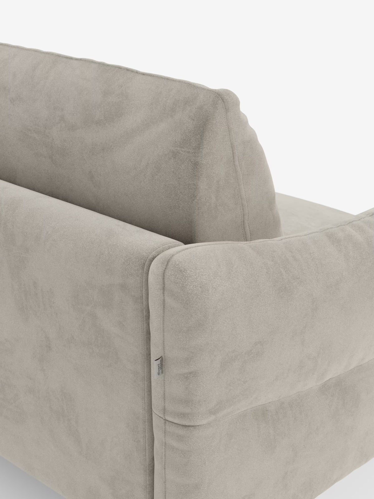 Un primo piano del divano letto Dalia in beige chiaro a 2, 3 e 4 posti con materasso H18 di Divani.Store mette in risalto il suo moderno tessuto in vellutino T30 resistente alle macchie. Lo schienale e i braccioli sono ripresi in un'inquadratura obliqua su sfondo bianco, mettendo in risalto il morbido rivestimento dalla trama delicata e una piccola etichetta in tessuto visibile sulla cucitura del bracciolo.