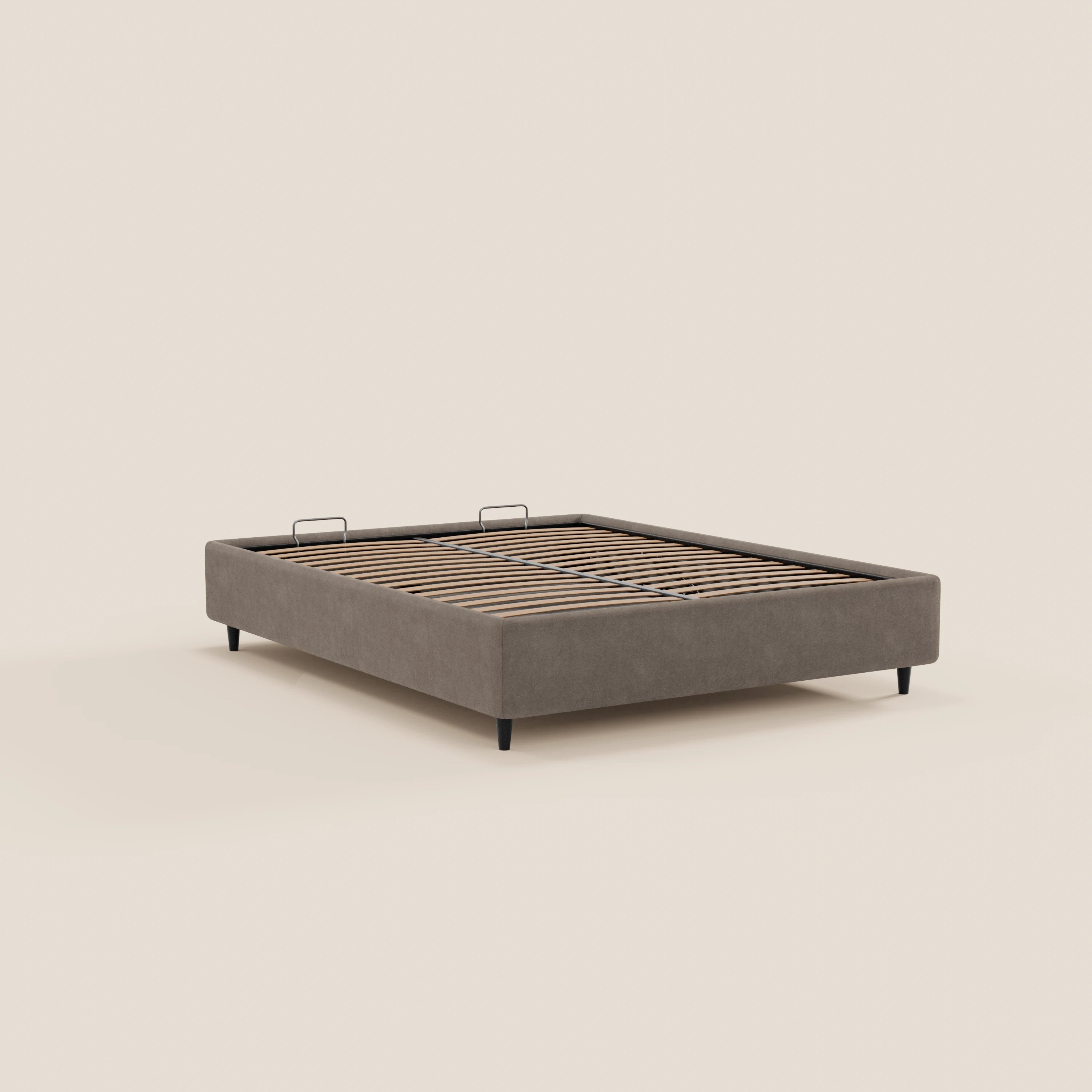 Il letto sommier imbottito ERON di Letti.store presenta un design moderno e dal profilo ribassato, con rivestimento in tessuto impermeabile color taupe certificato Oeko-Tex, gambe nere, doghe in legno a vista, due piccole maniglie nere e un vano portaoggetti. Sfondo bianco sporco a tinta unita.