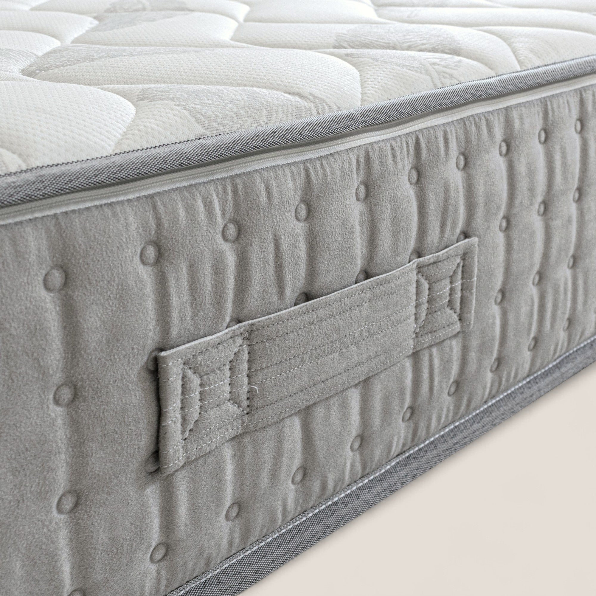 Primo piano di AERION - Materasso Ortopedico in Memory & Aquapur di Divani.Store, di colore grigio chiaro, che mostra la maniglia in tessuto sul lato trapuntato e la parte superiore bianca testurizzata, evidenziando il design pulito e ben imbottito per il comfort e il sostegno.