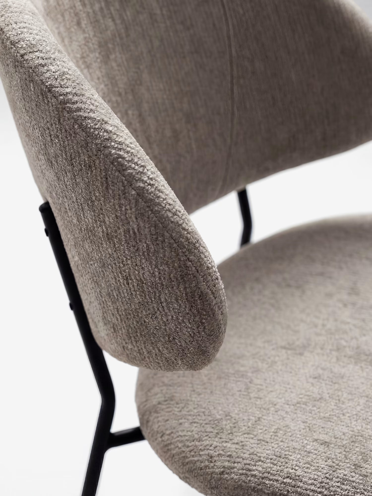 Primo piano della sedia Bruma di Divani.Store, caratterizzata da un elegante tessuto goffrato in beige chiaro, gambe in metallo nero e schienale avvolgente dal design minimalista su uno sfondo a tinta unita.