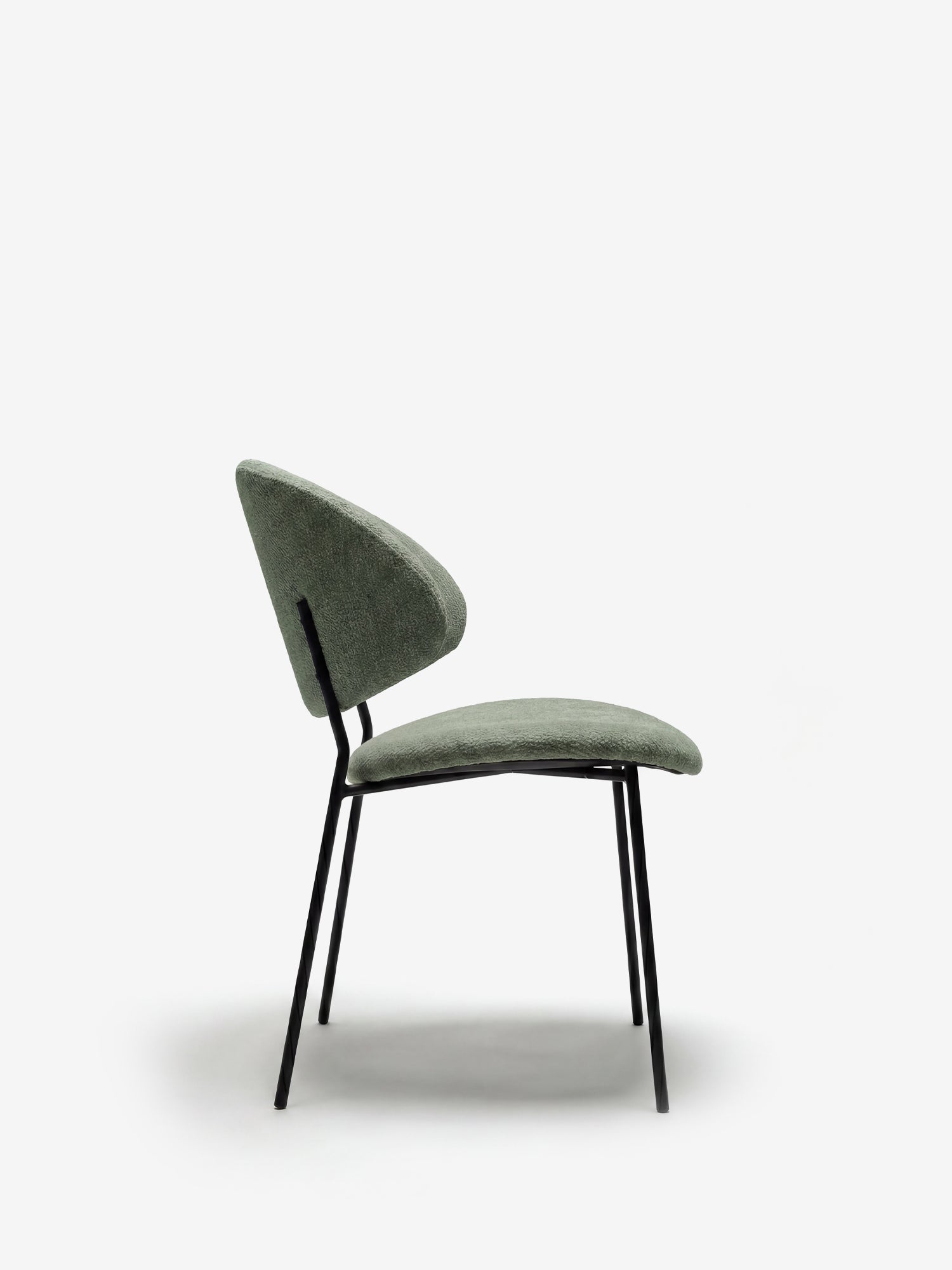 La sedia Bruma di Divani.Store, realizzata in elegante tessuto goffrato verde, presenta un design minimalista con schienale avvolgente e gambe sottili in metallo nero inclinate verso l’esterno. Immagine di profilo su sfondo bianco.