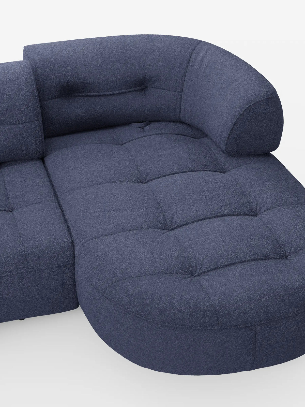 Un divano angolare Croissant blu, dalla forma a fagiolo, con schienali scorrevoli in morbido tessuto effetto cotone smacchiabile T33, con seduta trapuntata, silhouette sinuosa e design organico su uno sfondo grigio chiaro a tinta unita.