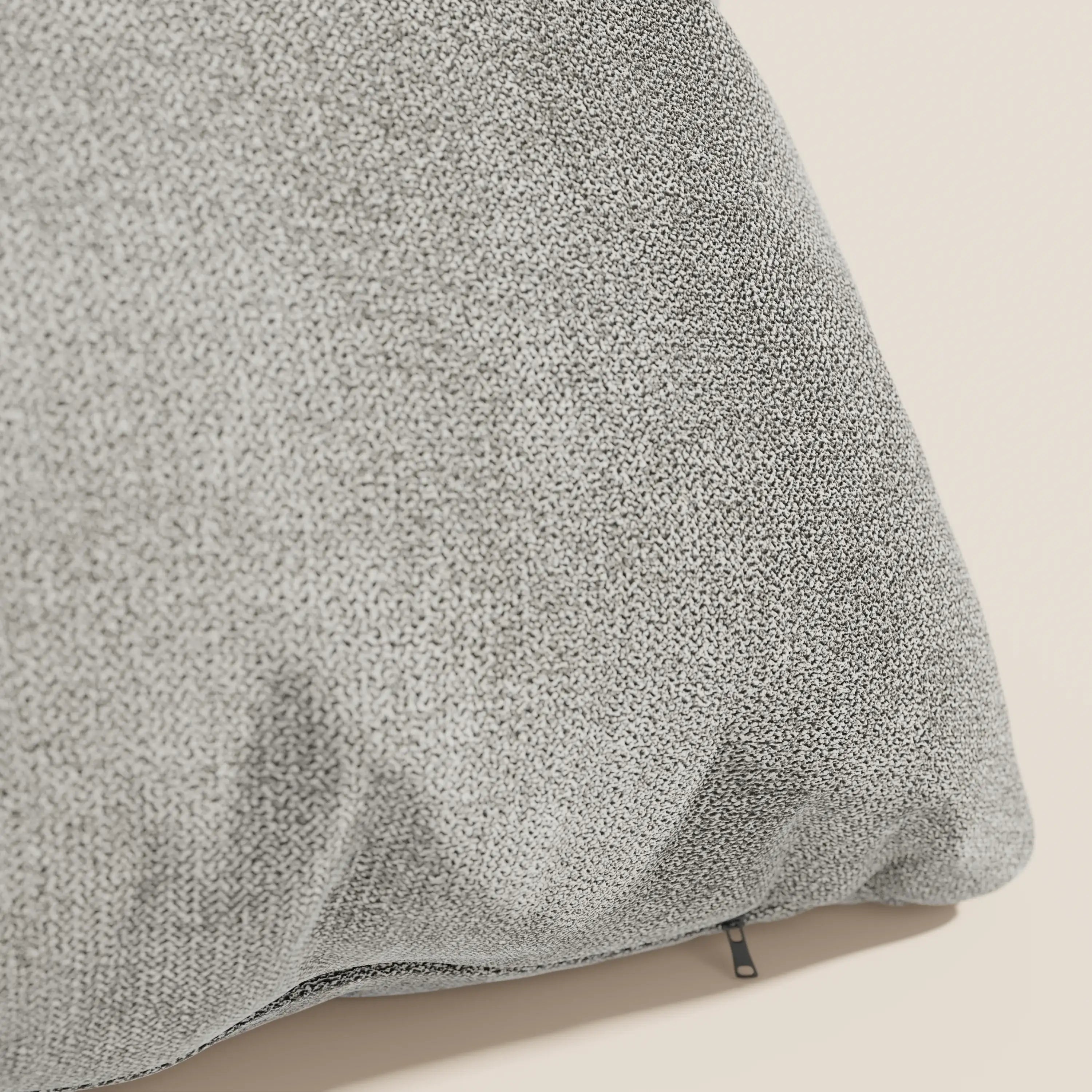 Primo piano del cuscino Destiny 45x45 cm di Divani.Store in morbido tessuto impermeabile T02 beige con trama a vista e piccola cerniera nera nell'angolo in basso a destra, appoggiato su una superficie beige chiaro.