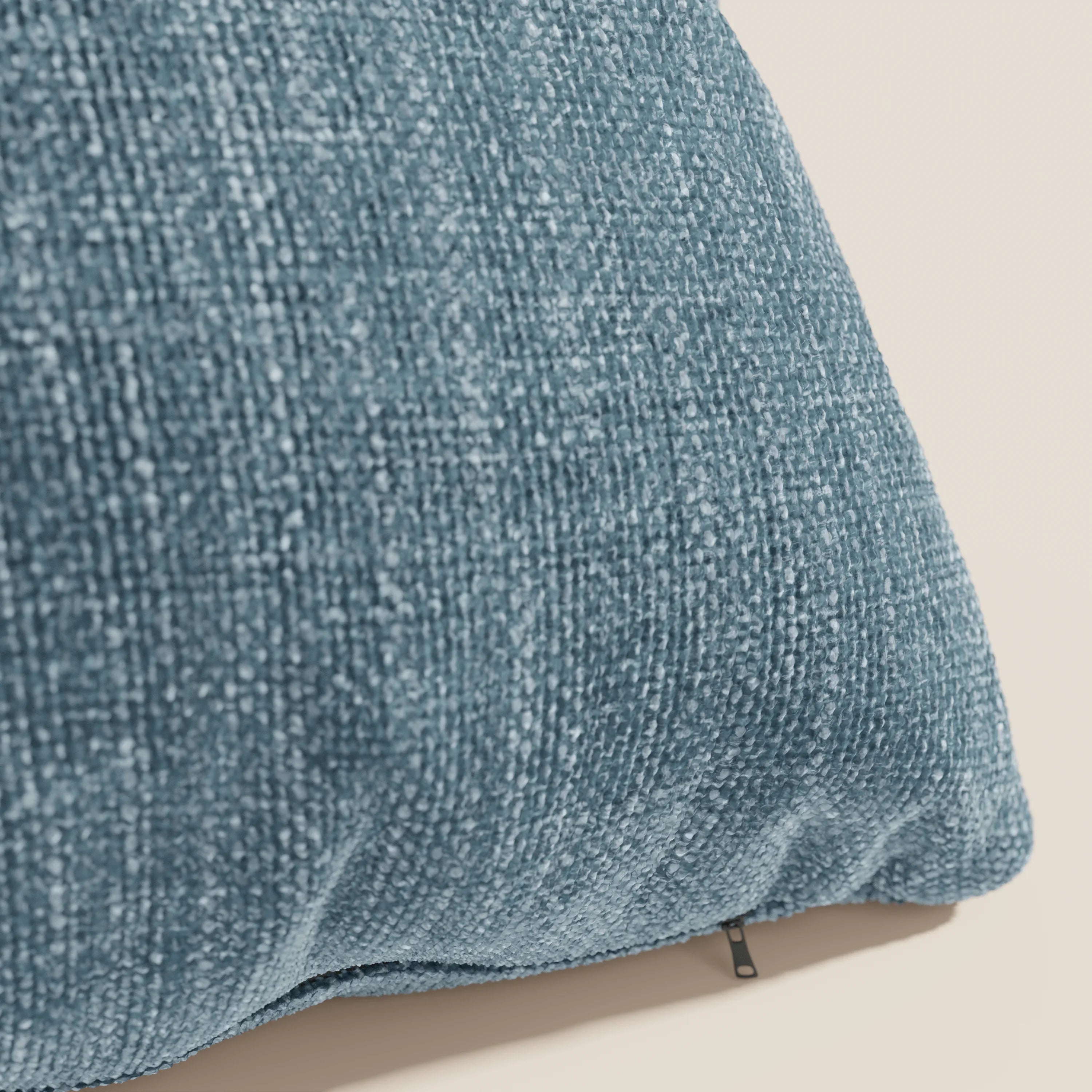Primo piano del cuscino Lyon di Divani.Store, presentato nel colore T06 azzurro. Realizzato in morbido tessuto intrecciato impermeabile, il suo tessuto blu rivela fili sottili e una sottile lucentezza. Sul bordo inferiore compare un piccolo tiretto nero.