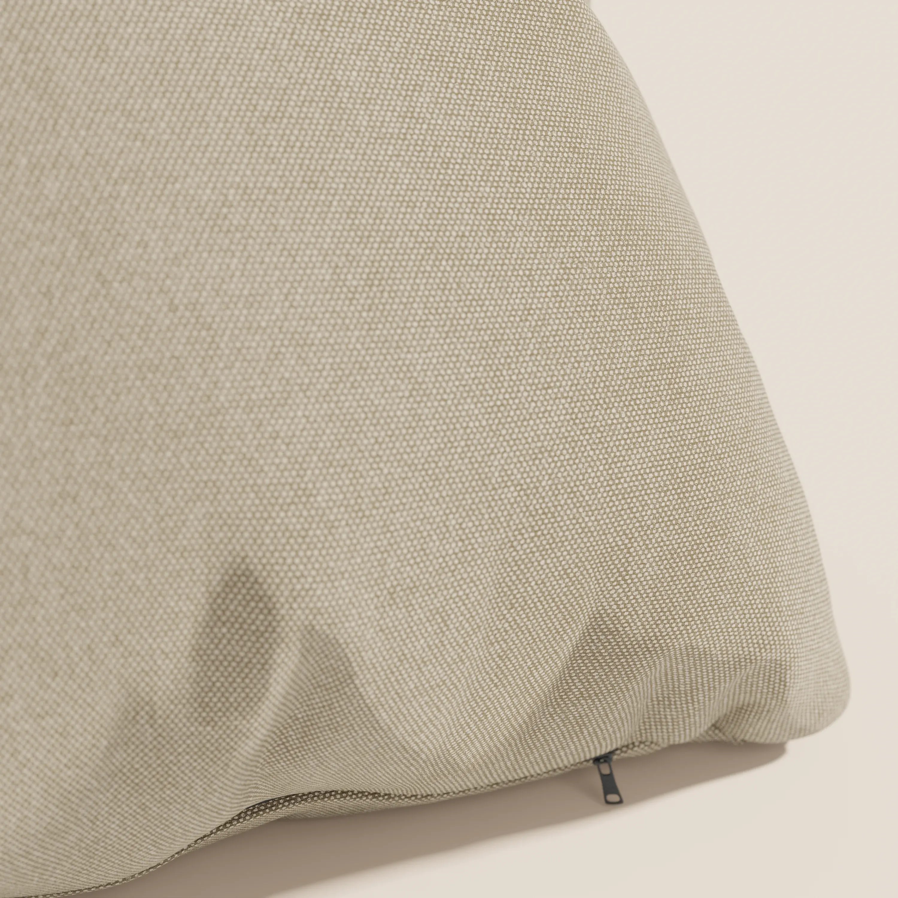 Primo piano del cuscino Honey di Divani.Store, in tessuto simil cotone impermeabile T13 beige, dimensioni 45x45. Le pieghe sottili e la cerniera nera aggiungono dettagli al suo aspetto fine e intrecciato su uno sfondo chiaro.