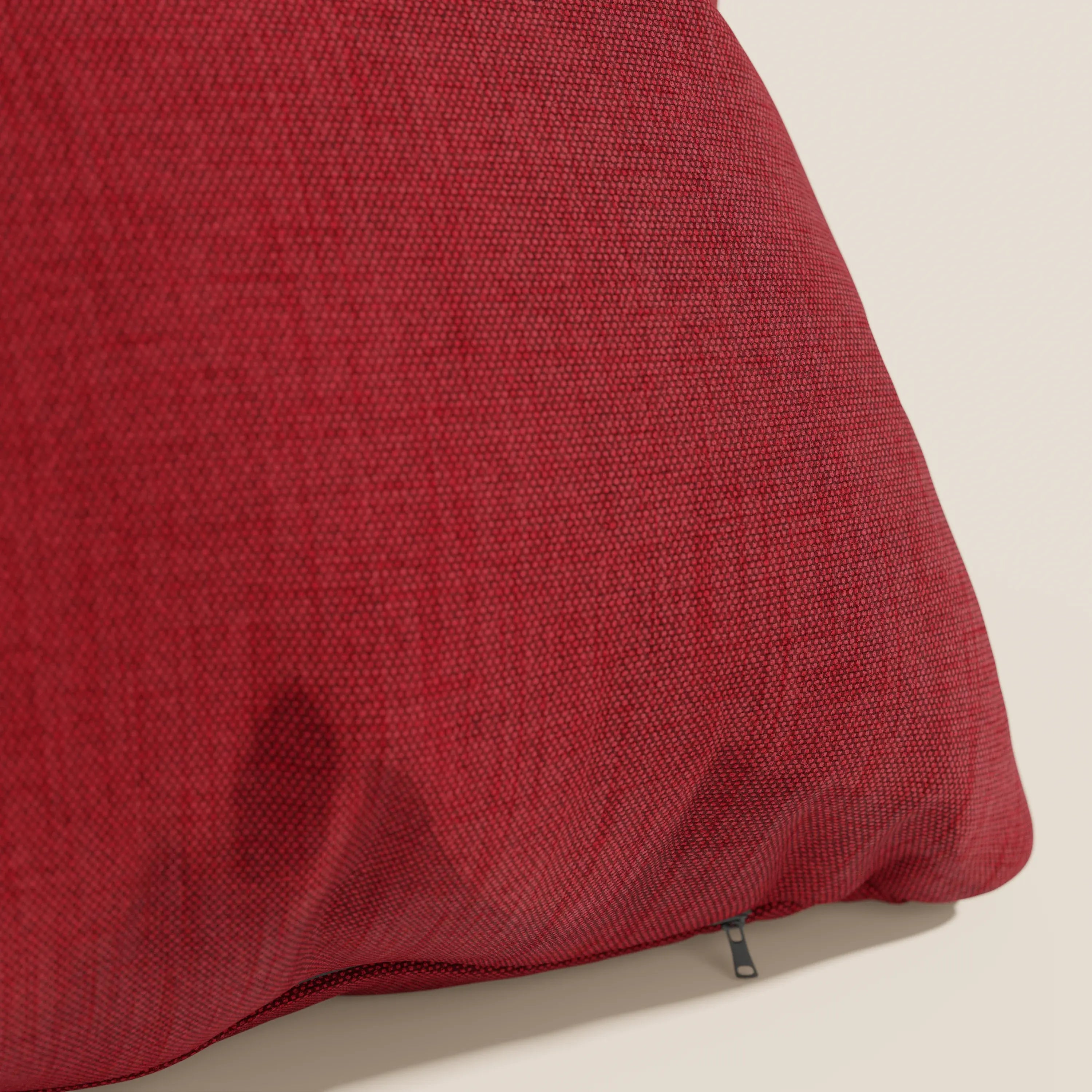 Un primo piano del cuscino Honey 45x45 impermeabile in rosso di Divani.Store, realizzato in tessuto similcotone T13 rosso, è mostrato su uno sfondo beige chiaro con una cerniera nera a vista che ne evidenzia l'aspetto felpato.