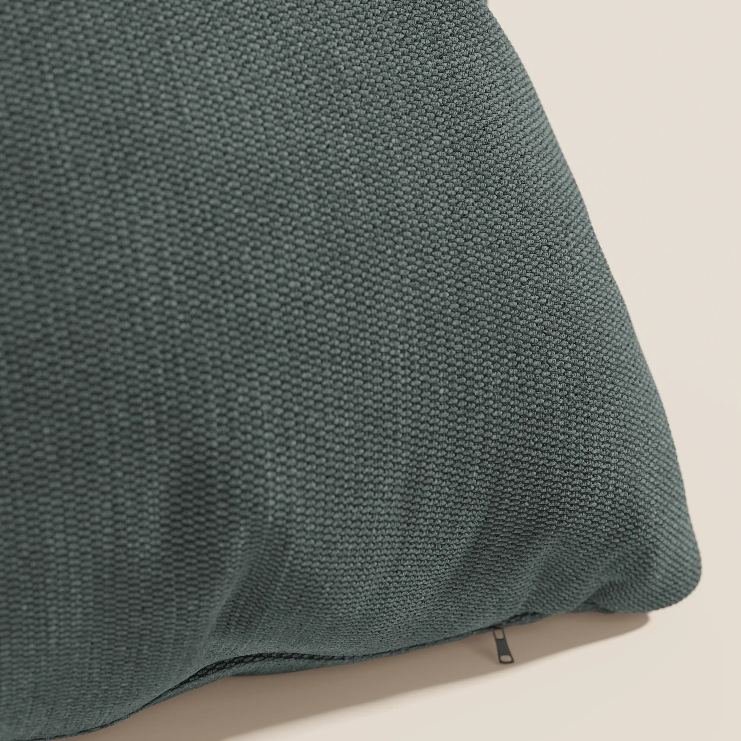 Primo piano del cuscino Miami 45x45 cm di Divani.Store in verde T14, realizzato in morbido tessuto impermeabile. Il rivestimento sfoderabile è dotato di una cerniera a vista. Solo una parte del cuscino testurizzato è mostrata su uno sfondo a tinta unita.