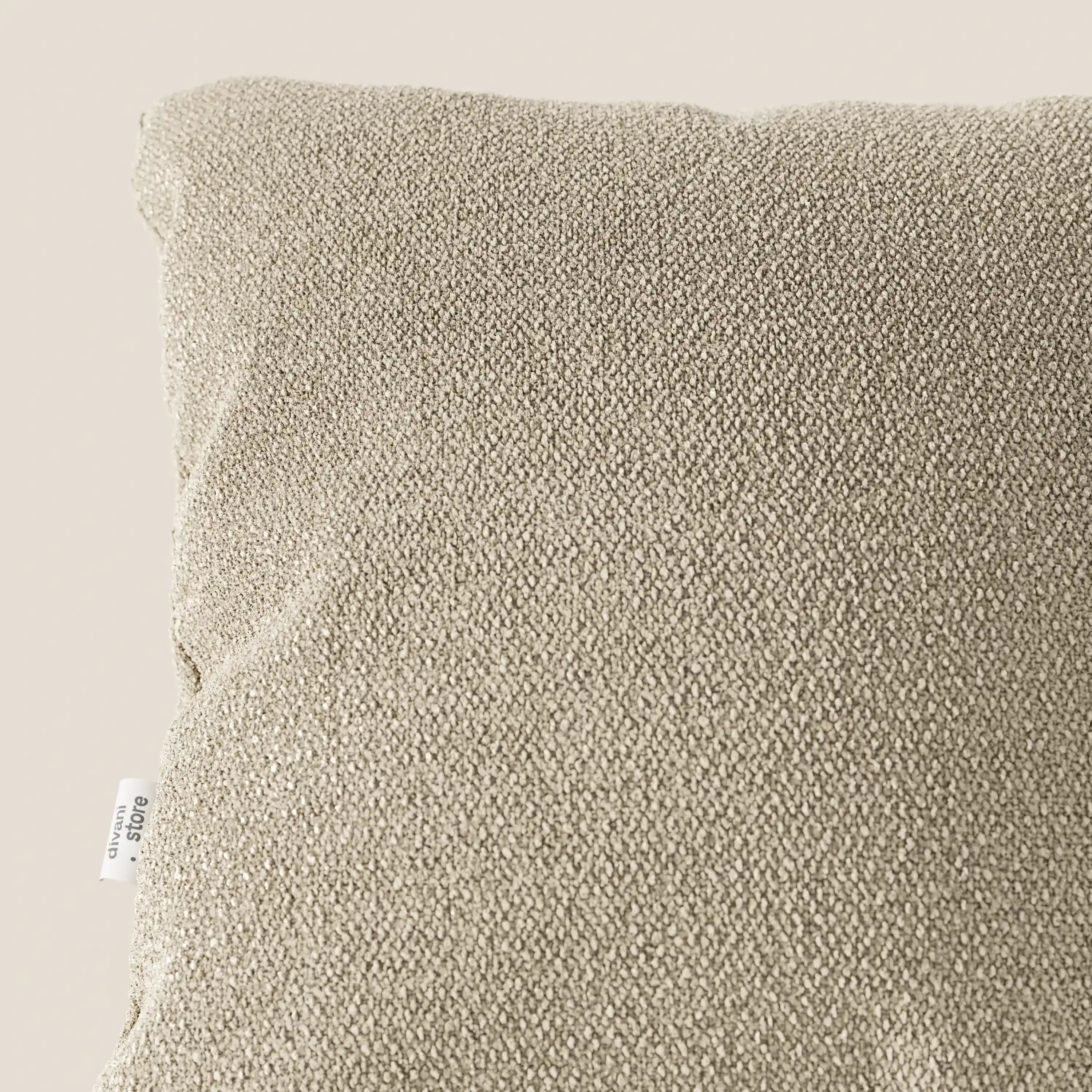 Primo piano del cuscino Lambada di Divani.Store in beige, realizzato in tessuto T33 fresco, antimacchia e impermeabile, simile al cotone. La consistenza morbida e la piccola etichetta bianca sul bordo sinistro sono visibili su uno sfondo chiaro.