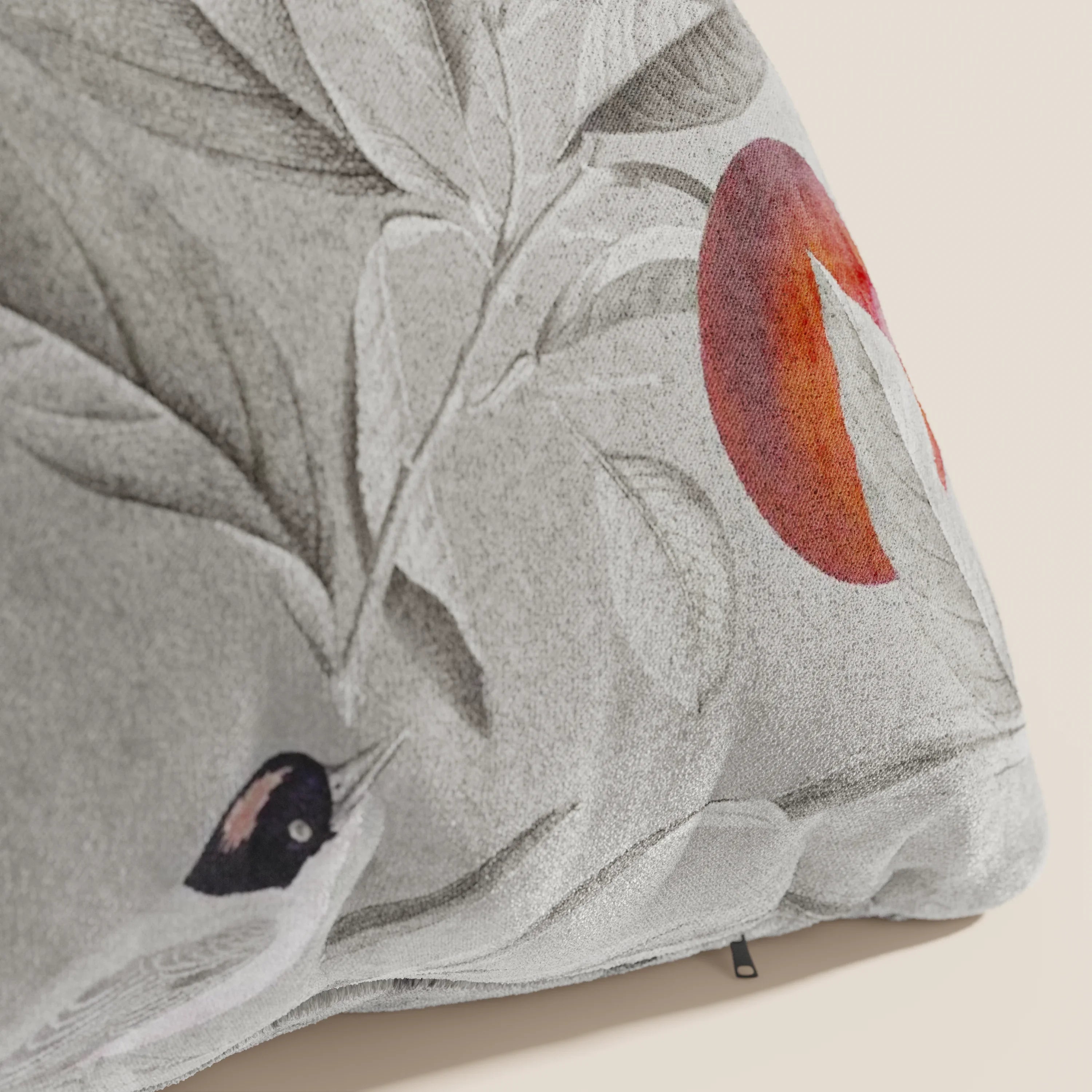 Primo piano del cuscino Lemon elegante a fantasia in velluto impermeabile grigio di Divani.Store, caratterizzato da un disegno ispirato alla natura con un uccello bianco e nero, grandi foglie grigie e un frutto rosso arancio su uno sfondo chiaro.