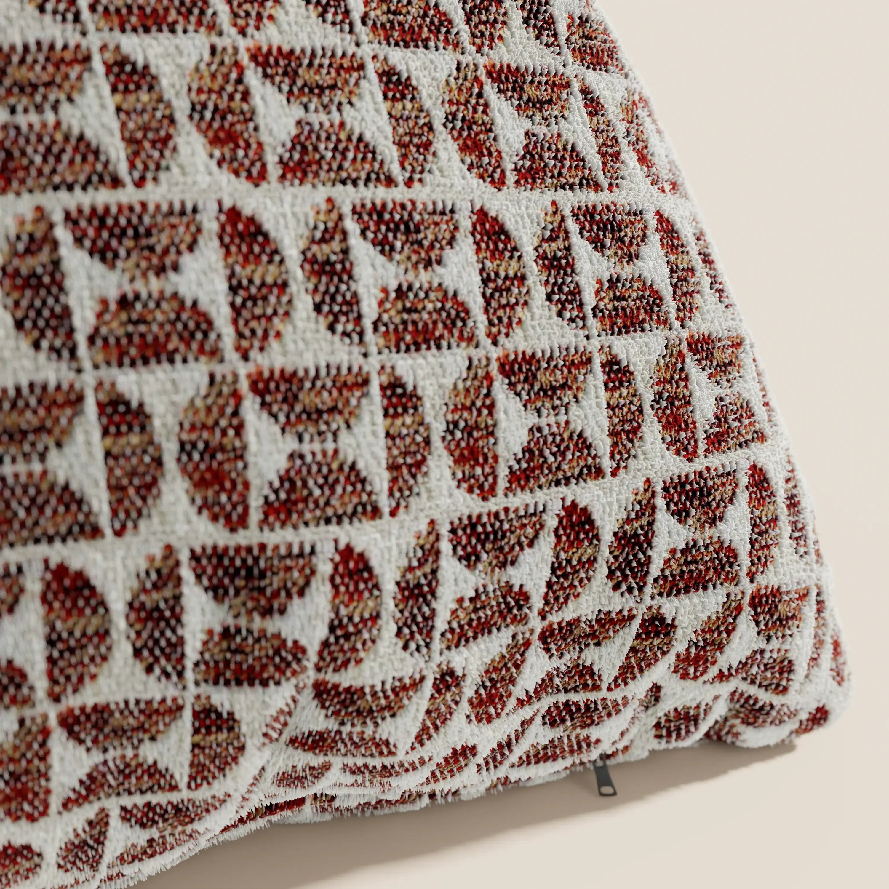 Primo piano del cuscino Naxos Decoro 45x45 in lino di Divani.Store, che mostra il suo elegante motivo geometrico nei toni del rosso e del marrone su fondo crema. Il cuscino quadrato è ripreso di profilo, mettendo in risalto parte del tirazip in metallo nella parte inferiore.