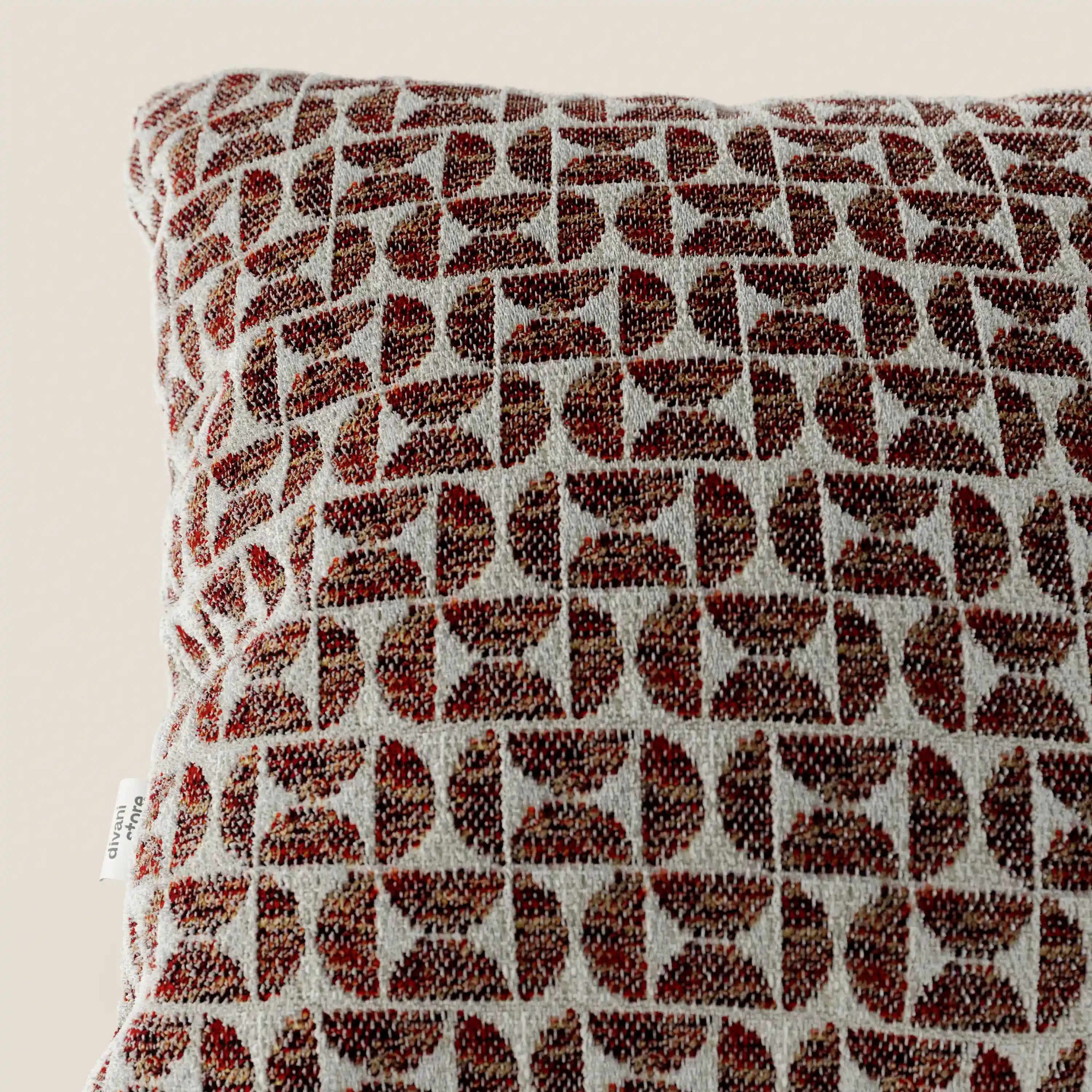 Un primo piano del cuscino Naxos Decoro 45x45 in lino di Divani.Store mette in risalto il suo elegante motivo geometrico a semicerchio nei toni del marrone e del rosso ruggine su sfondo beige. Il lino testurizzato e una piccola etichetta bianca sul bordo sinistro ne esaltano il fascino decorativo.