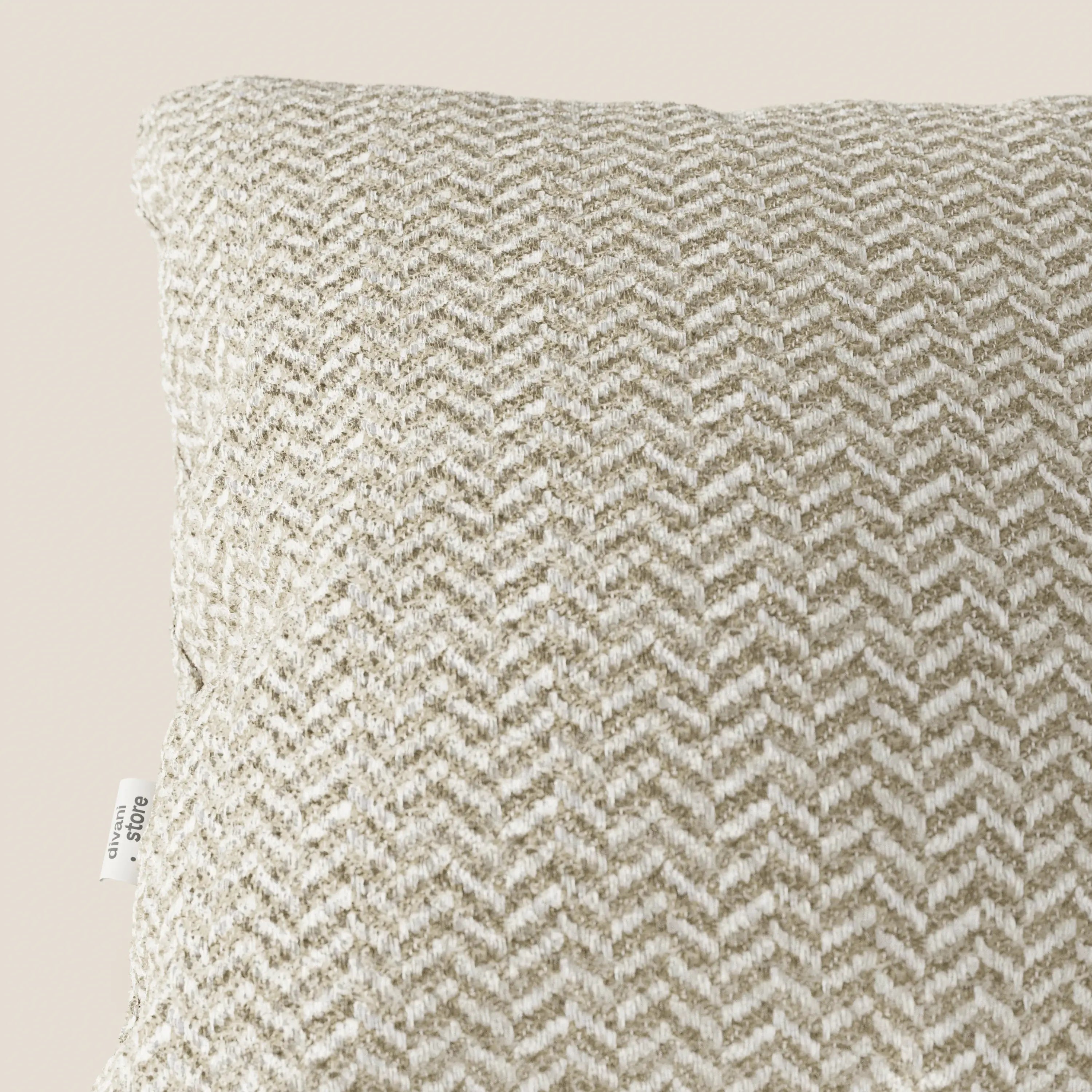 Un primo piano del cuscino Sorrento 45x45 in Lino di Divani.Store ne mette in risalto la trama a chevron nei toni del beige e del bianco, il tessuto testurizzato e la piccola etichetta laterale. Questo elegante cuscino, lavabile in lavatrice, spicca su uno sfondo bianco sporco.