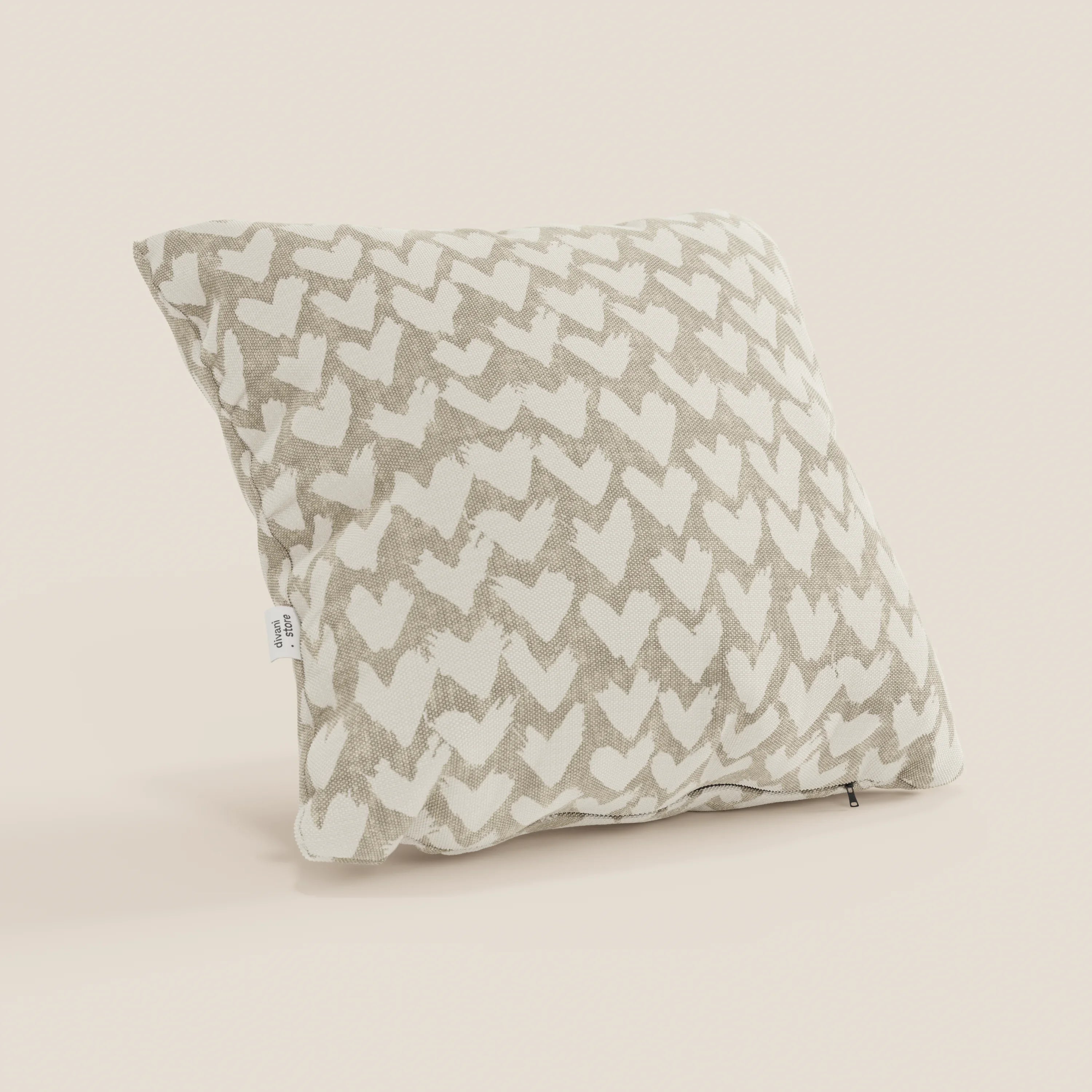 Il cuscino geometrico Arrow di Divani.Store è un cuscino decorativo quadrato, beige, idrorepellente, con un disegno a freccia a spina di pesce bianco sporco, una piccola etichetta bianca e una cerniera visibile nell'angolo inferiore.