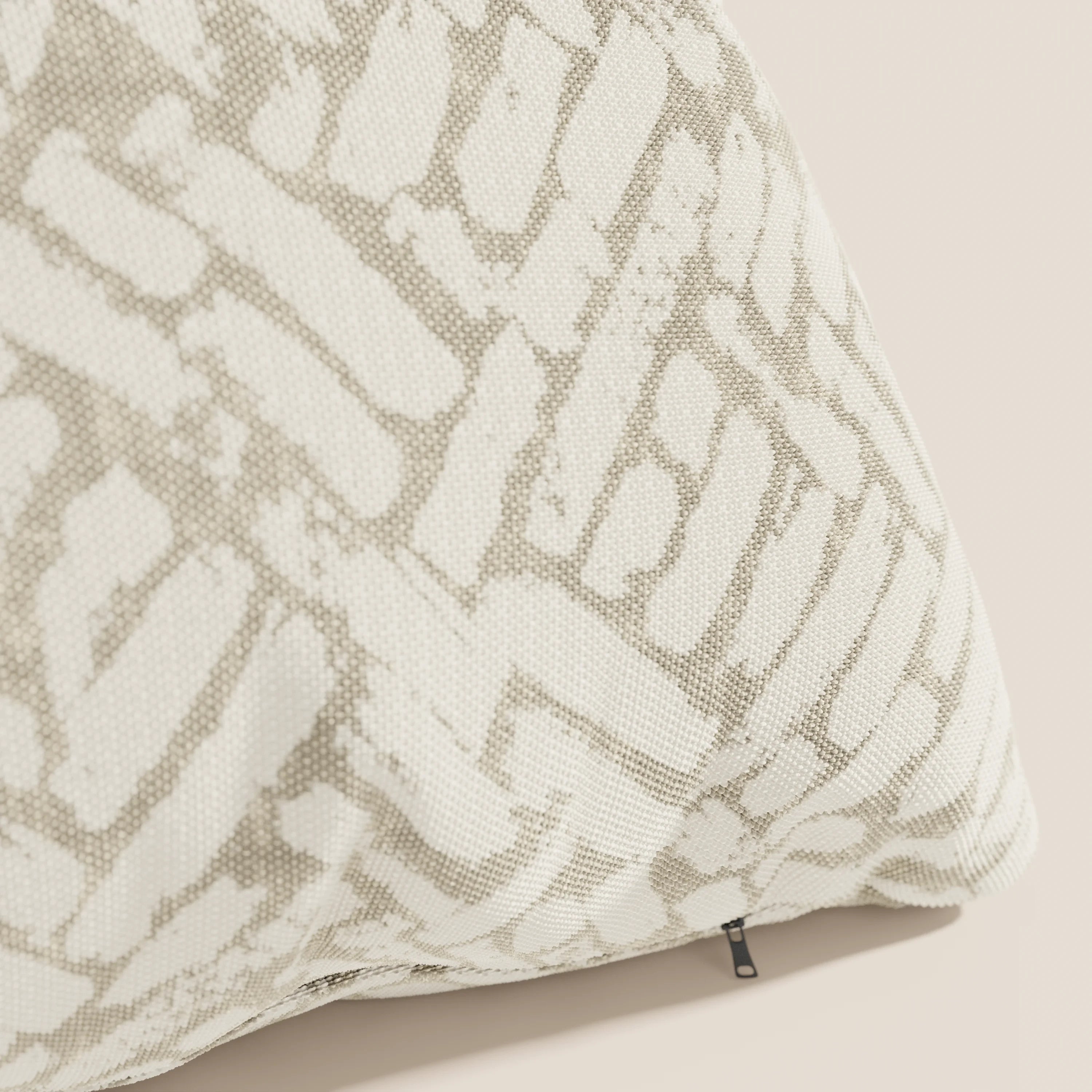 Primo piano del cuscino geometrico Brick di Divani.Store, realizzato in tessuto idrorepellente beige con un motivo astratto bianco e grigio chiaro e una piccola etichetta nera sul bordo inferiore.