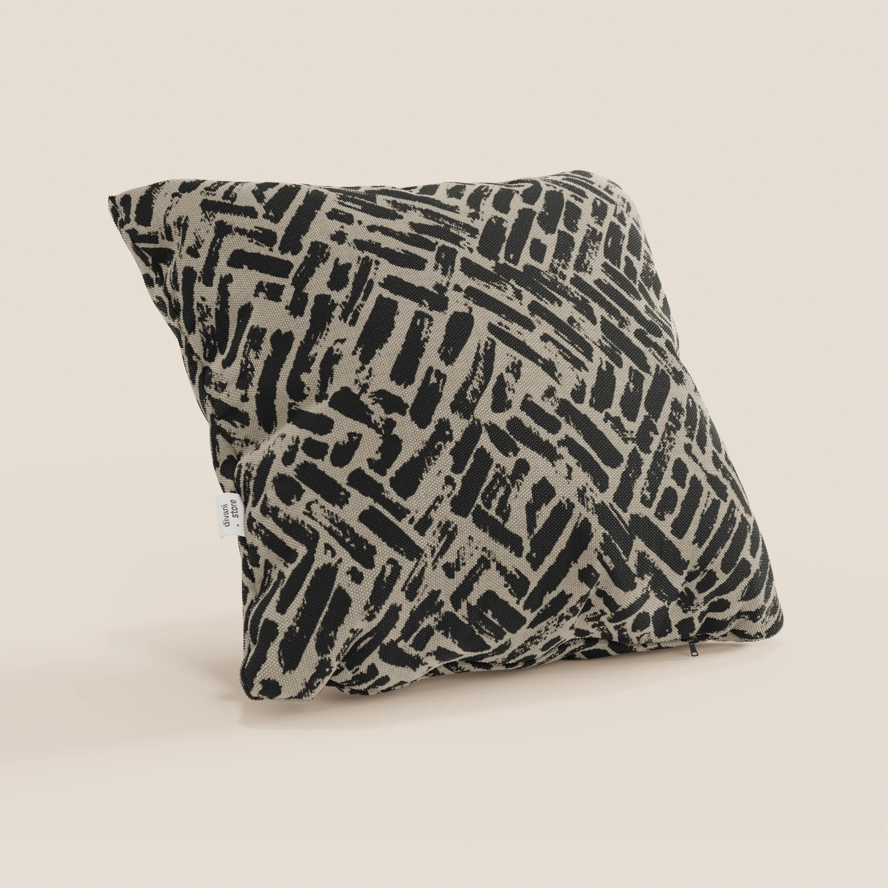 Il cuscino geometrico Brick di Divani.Store, realizzato in tessuto tortora idrorepellente, è caratterizzato da un'audace fantasia astratta nera su sfondo beige ed è presentato leggermente inclinato con un cartellino in tessuto bianco su una superficie chiara.