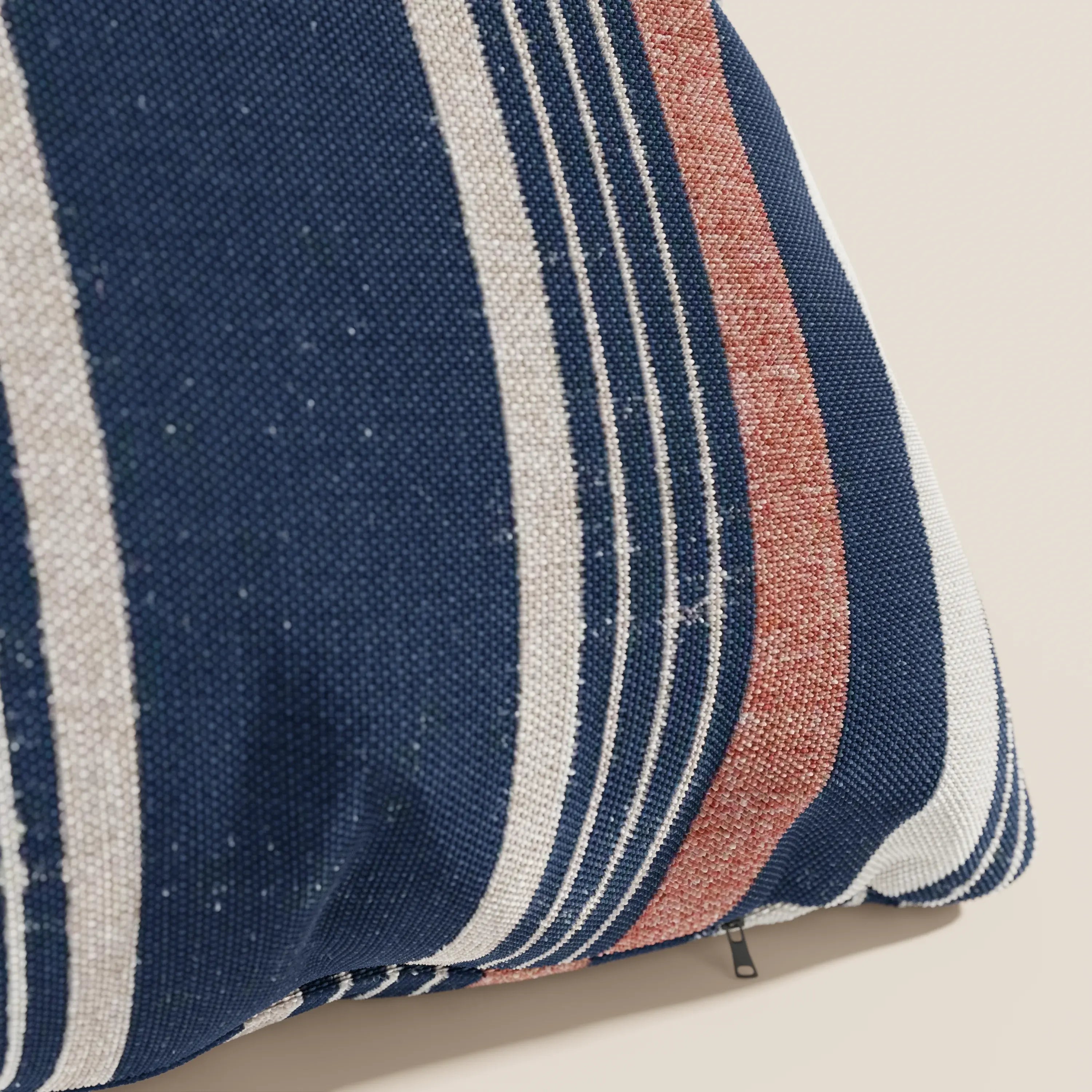 Primo piano di un cuscino a fantasia rigata 45x45 di Divani.Store, in tessuto impermeabile arancio, caratterizzato da ampie strisce blu, bianche e rosso ruggine di spessore variabile. Una piccola cerniera è visibile su uno sfondo beige chiaro.