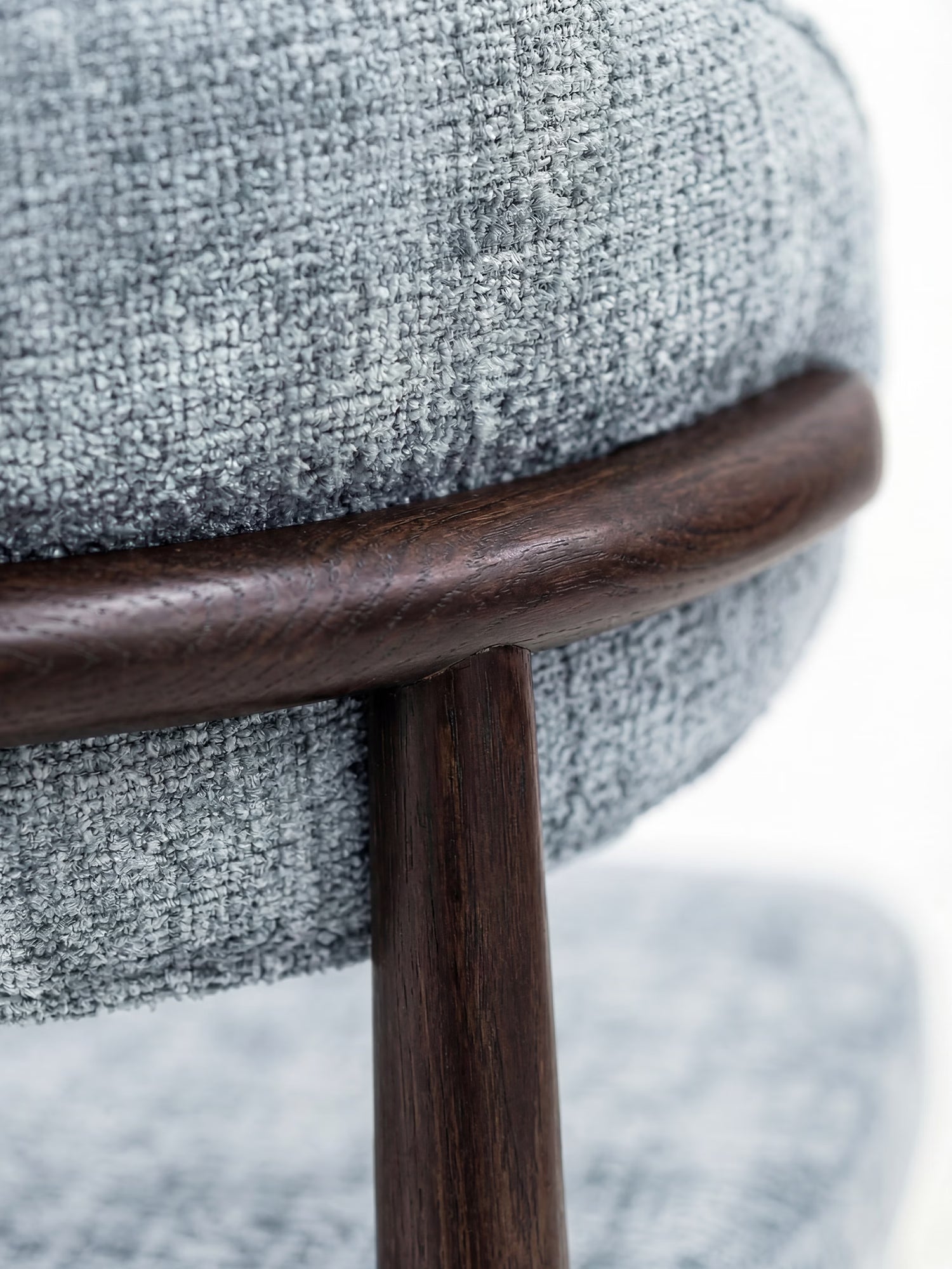 Primo piano del modello “Dafne Sedia” imbottito di Divani.Store, realizzato in ciniglia OEKO-TEX® grigio chiaro e con struttura in legno massello wengé e schienale arrotondato; l’attenzione è focalizzata sul punto di giunzione tra il supporto e la seduta imbottita e curvata.