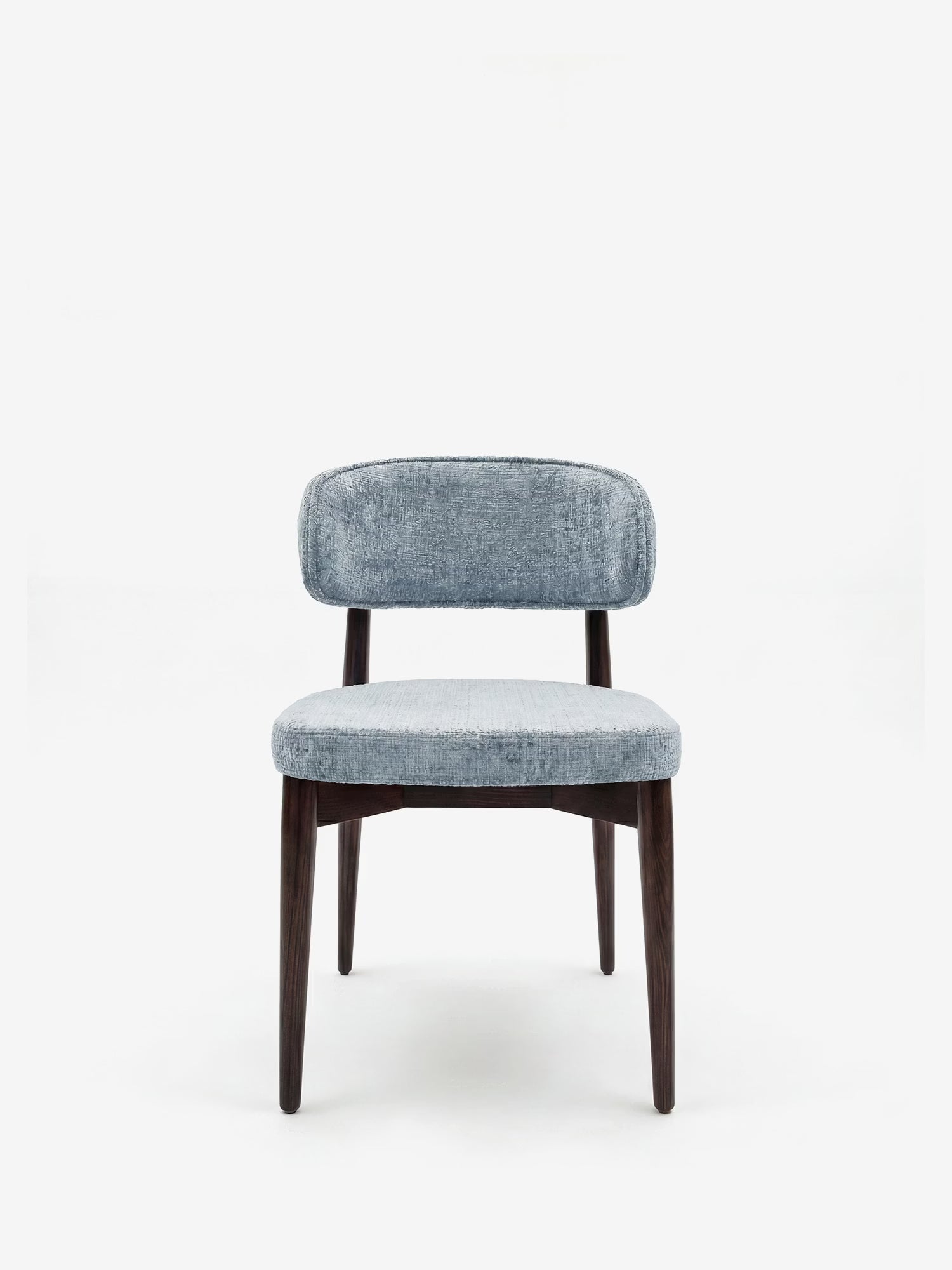 La sedia Dafne di Divani.Store presenta uno schienale curvo e imbottito in tessuto ciniglia azzurro certificato OEKO-TEX® e quattro gambe in legno massello wengé. Il design moderno di questa sedia è caratterizzato da uno sfondo bianco a tinta unita, rivolto in avanti.