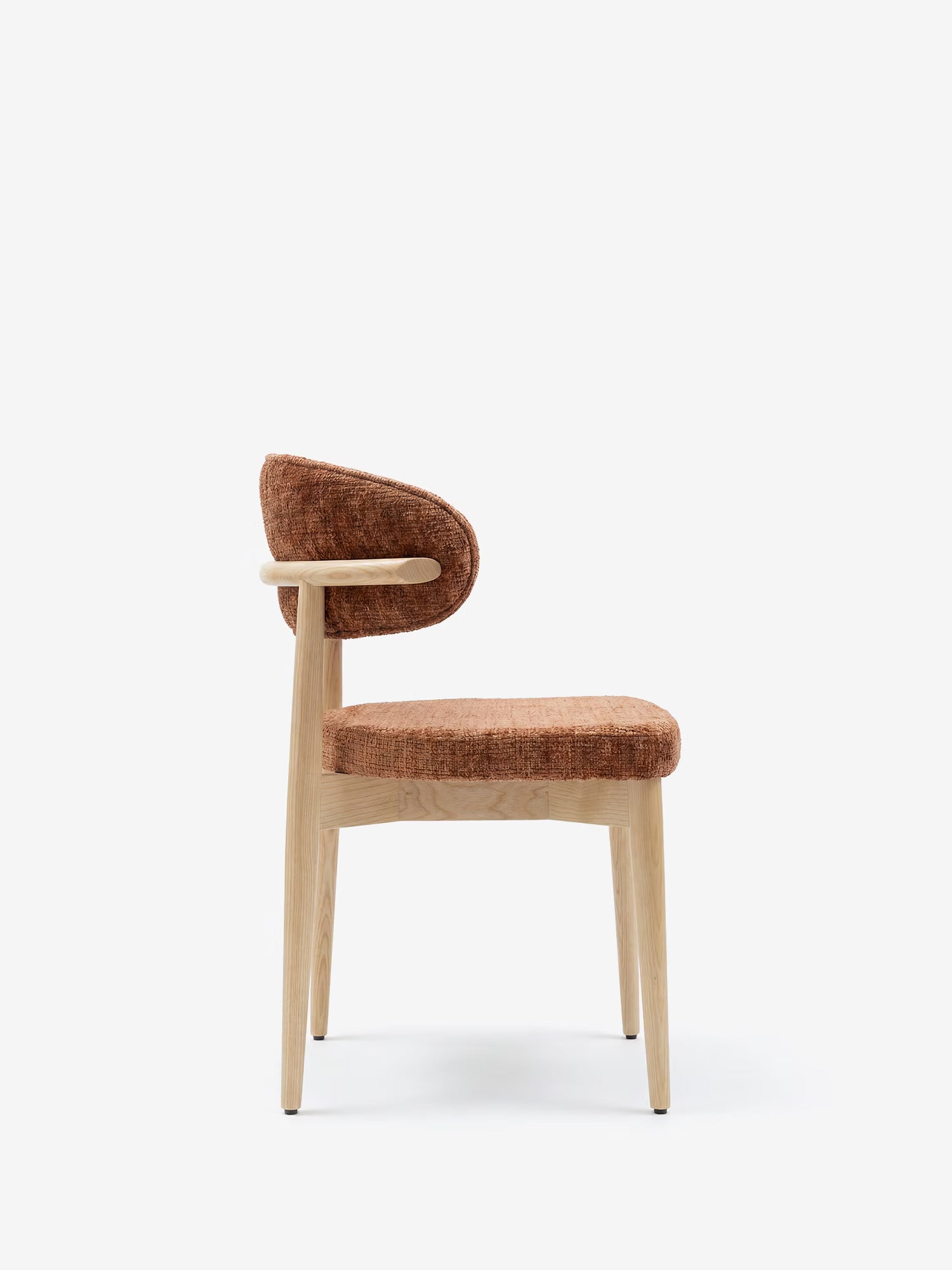 La sedia Dafne di Divani.Store presenta gambe e struttura in rovere massello naturale, con schienale curvo e seduta rivestiti in ciniglia color ruggine certificata OEKO-TEX®. Immagine di profilo su sfondo bianco a tinta unita.