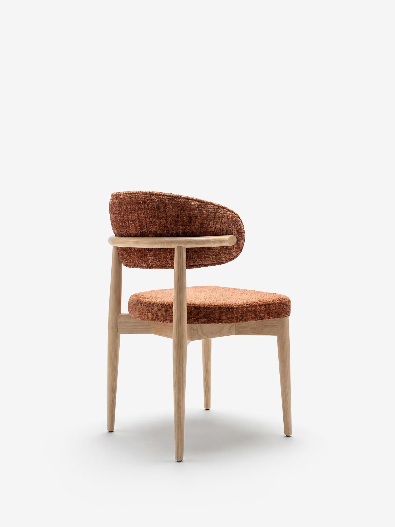 La sedia imbottita Dafne di Divani.Store presenta gambe e struttura in rovere naturale massiccio, uno schienale curvo e un rivestimento in ciniglia certificato OEKO-TEX® color ruggine, che ne esalta il design elegante e minimalista su uno sfondo bianco a tinta unita.