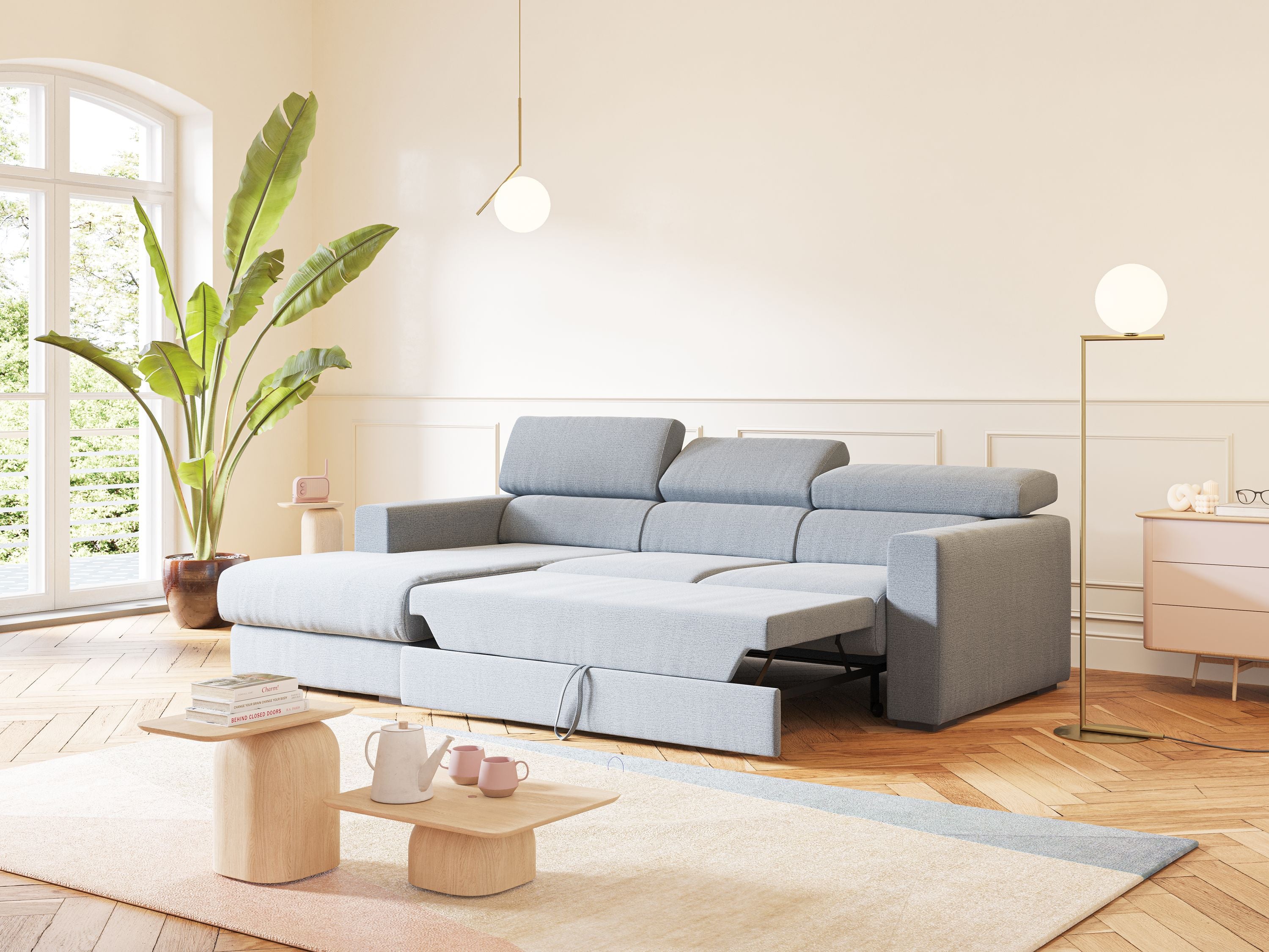 Un soggiorno moderno con il divano angolare Dylan con estraibile a cassettone in tessuto T19 carta da zucchero di Divani.Store, chaise lounge allungabile, pareti chiare, pavimenti a spina di pesce, pianta alta, luce a sospensione, tappeto chiaro, tavolo in legno e tazze rosa.