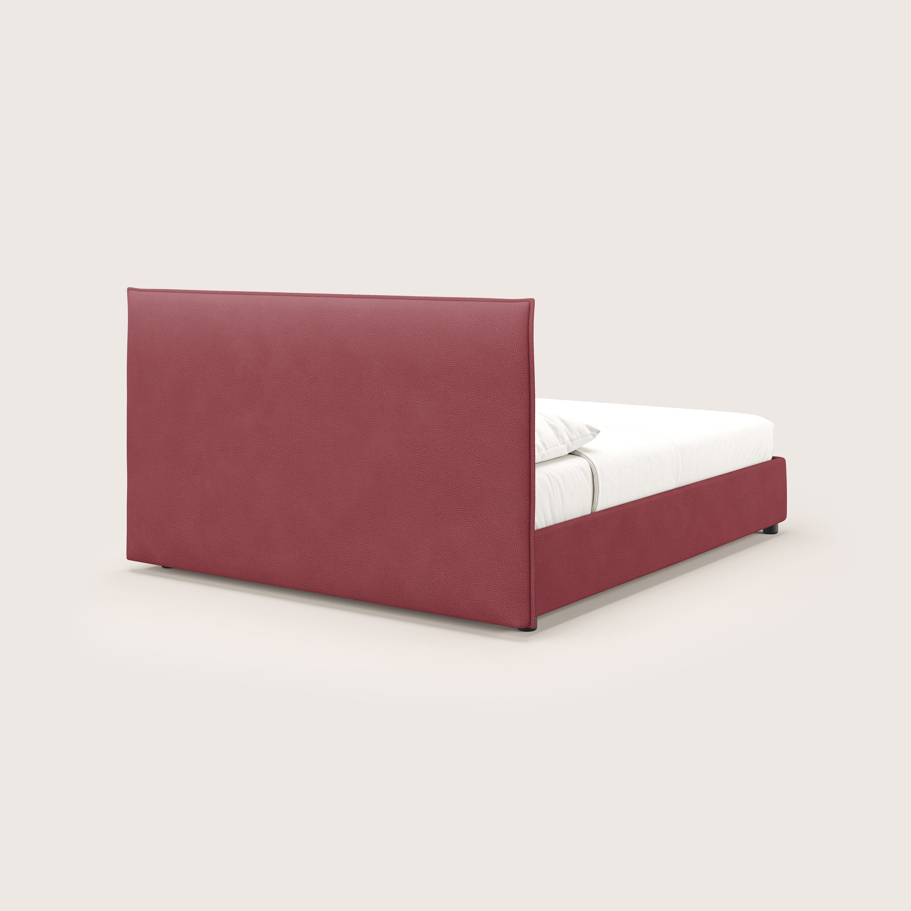 Nina letto contenitore di Letti.store: un letto dal design minimale in microfibra rossa antimacchia effetto pelle, con testata e base imbottite di forma rettangolare alta e biancheria da letto bianca, visto da un'angolazione laterale posteriore su uno sfondo grigio chiaro.