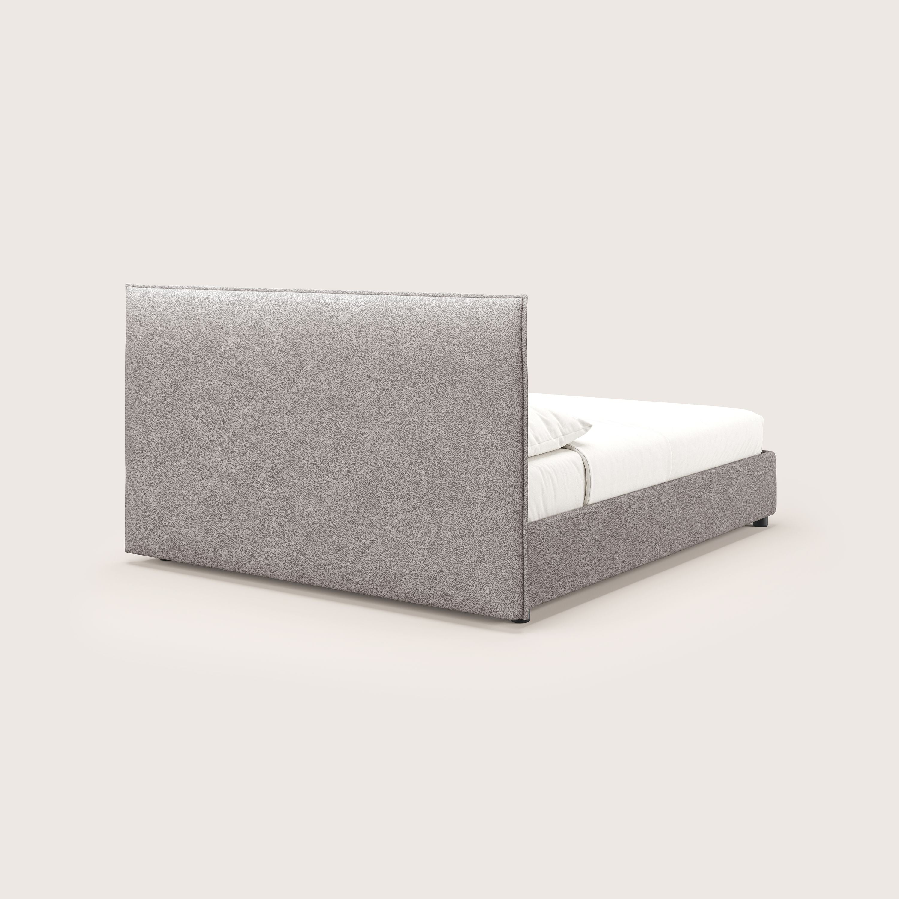 Il letto contenitore Nina di Letti.store è caratterizzato da un design minimale in microfibra antimacchia color tortora con un'alta testiera rettangolare imbottita e una struttura abbinata, mostrata con biancheria da letto bianca e due cuscini da una vista laterale posteriore angolata.