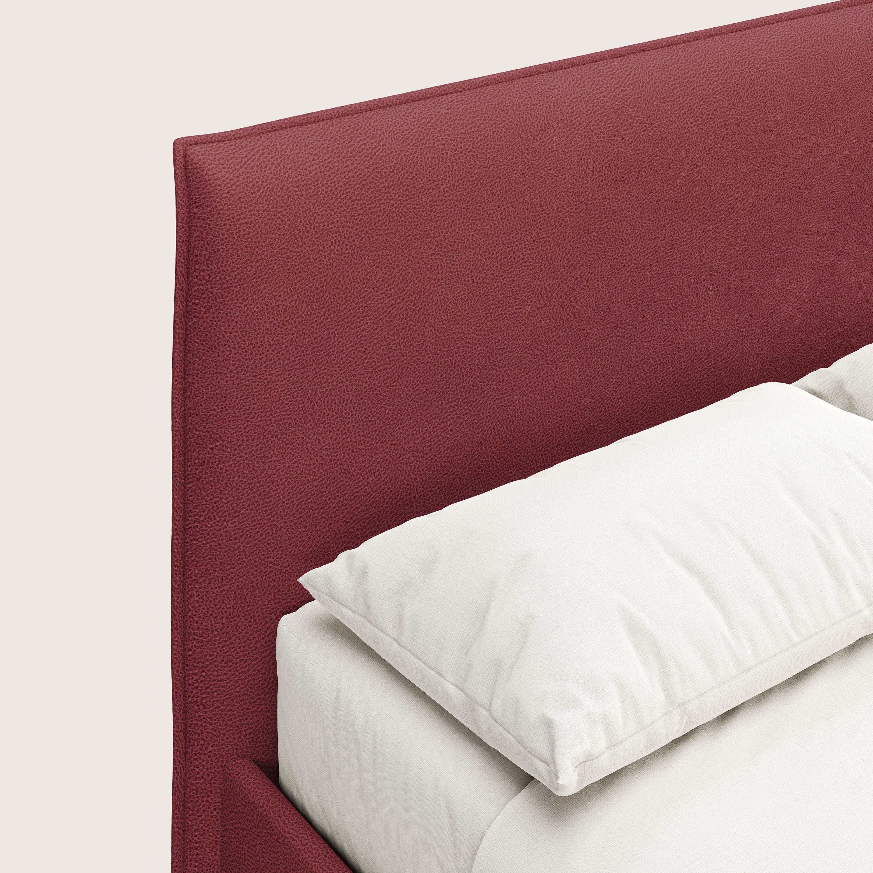 Primo piano di Nina letto contenitore di Letti.store, caratterizzato da un design minimale e da una testiera in microfibra effetto pelle rosso intenso e antimacchia, con biancheria da letto bianca e un unico cuscino su uno sfondo chiaro.