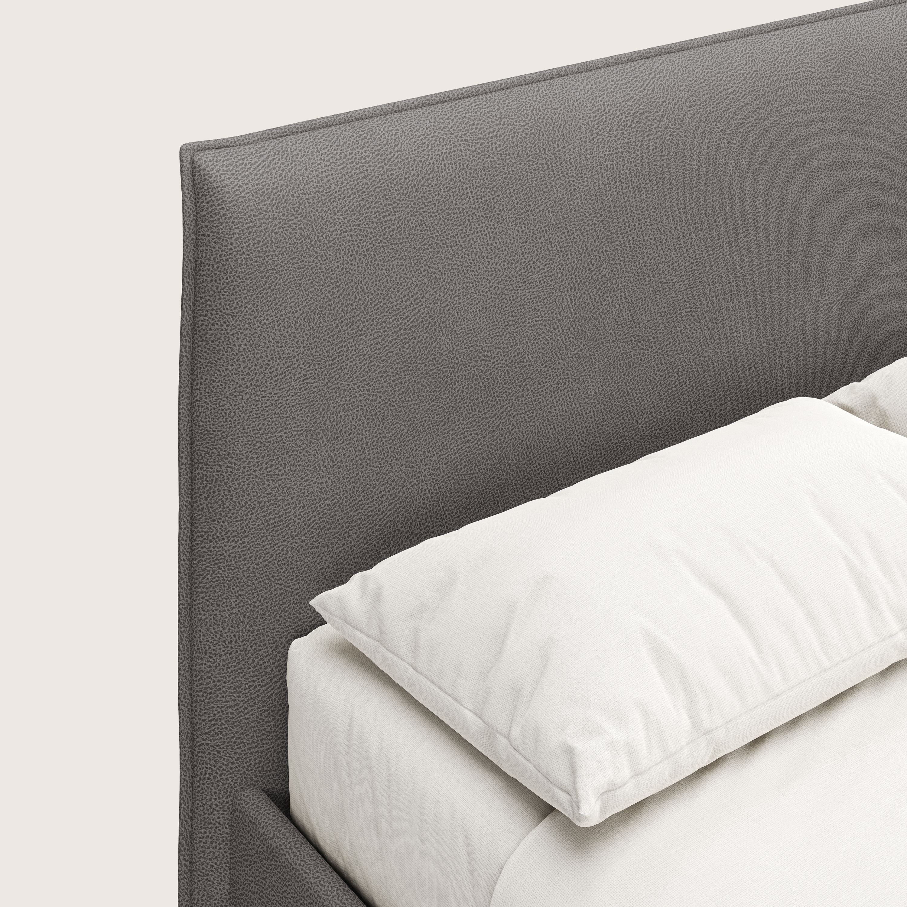 Un primo piano del letto contenitore Nina di Letti.store rivela un'alta testata in microfibra effetto pelle antracite e una biancheria da letto bianca, un'elegante dimostrazione di design italiano minimal.