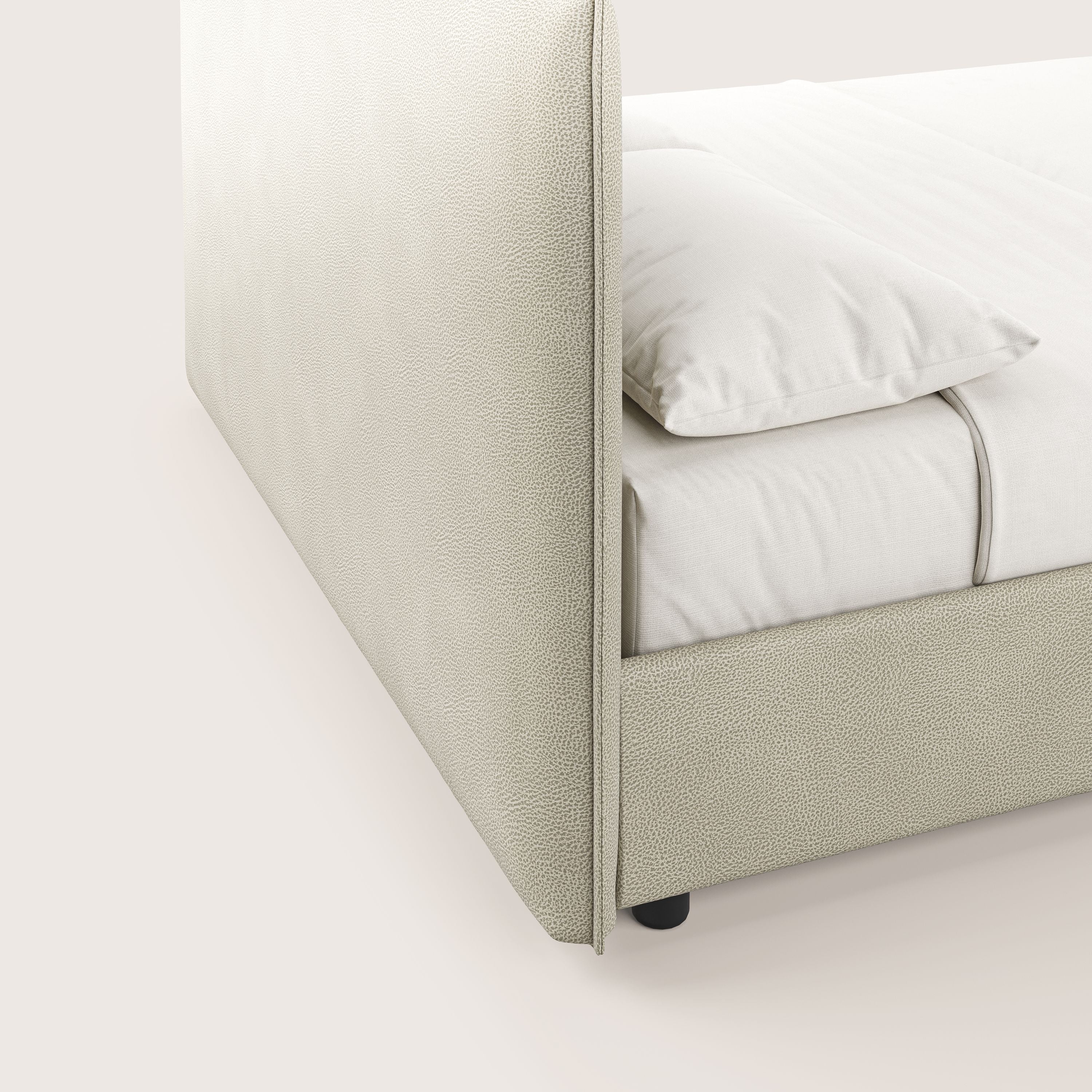 Un primo piano di Nina di Letti.store, un letto contenitore minimal in panna microfibra effetto pelle smacchiabile, mette in evidenza la testata alta, il tessuto chiaro, la biancheria da letto color crema e le piccole gambe scure su un pavimento neutro.