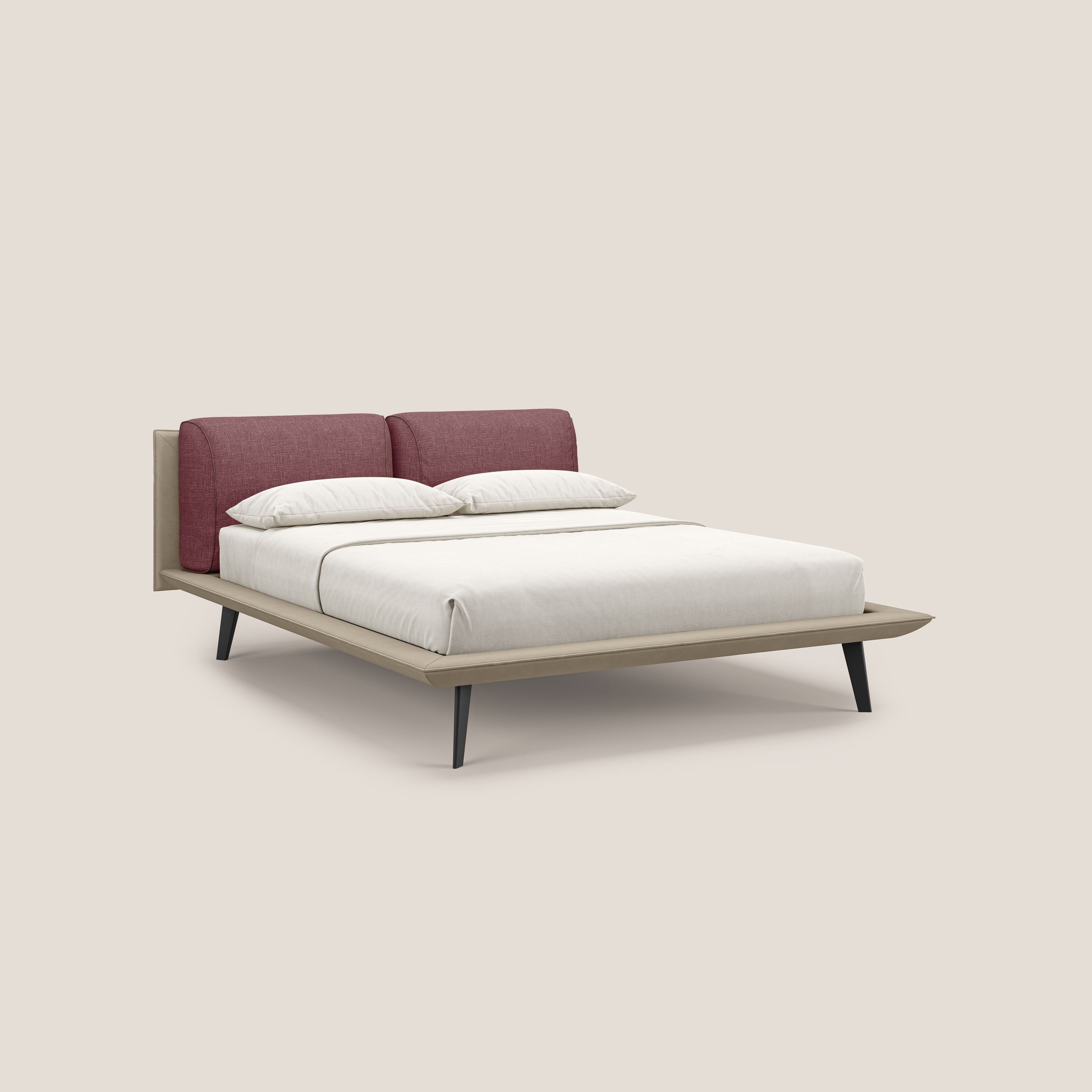Il letto di design Petra di Letti.store è caratterizzato da un tessuto impermeabile bicolore (T11 e T06 tortora-rosso), cuscini in piuma e piedi in mogano. È presentato con biancheria e cuscini bianchi su uno sfondo beige chiaro.