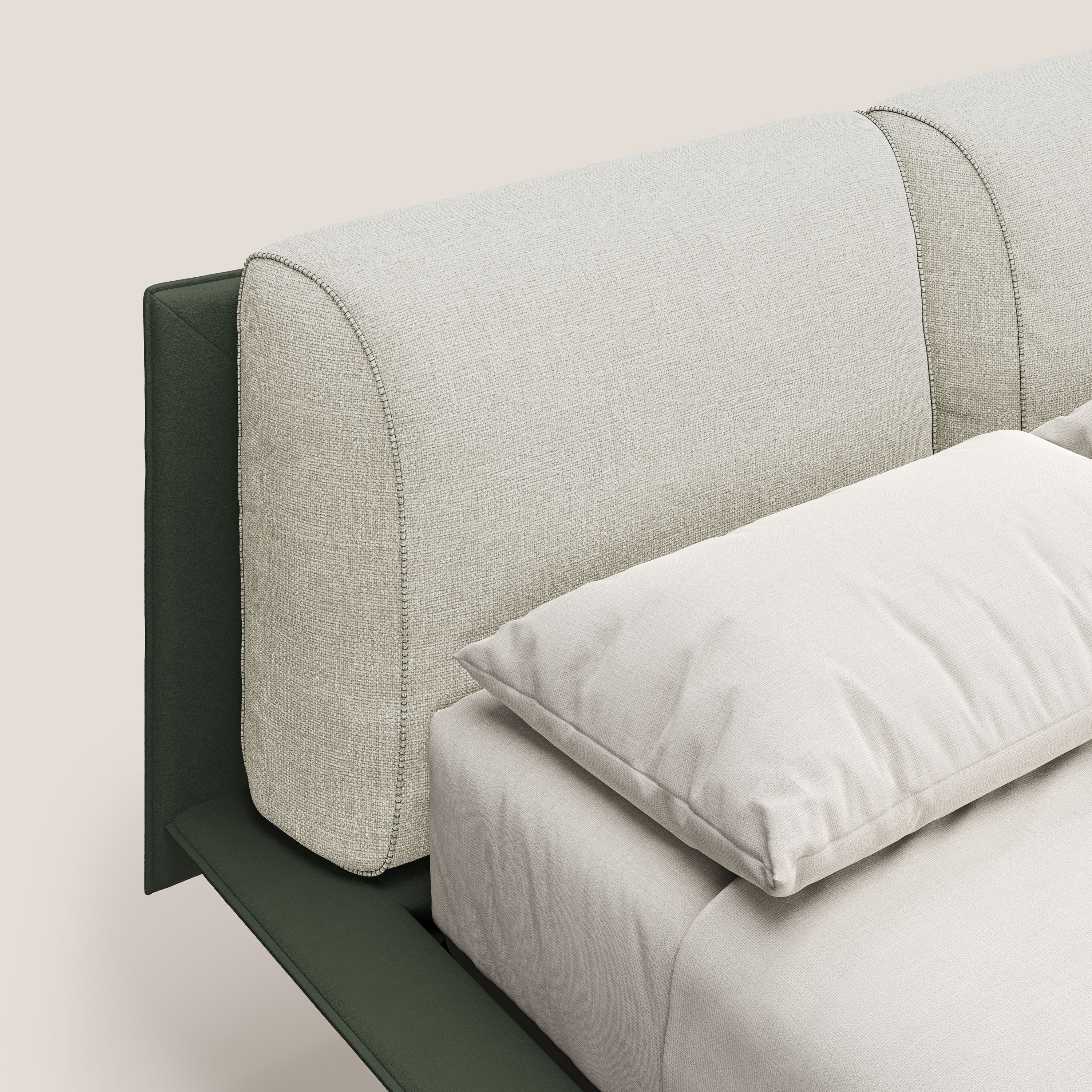 Un primo piano di Petra letto di design bicolore di Letti.store mostra una testiera in tessuto impermeabile verde e panna con cuscini in piuma, bordi curvi e piedini in mogano; abbinata a una base ortopedica a doghe che garantisce comfort e sostegno.