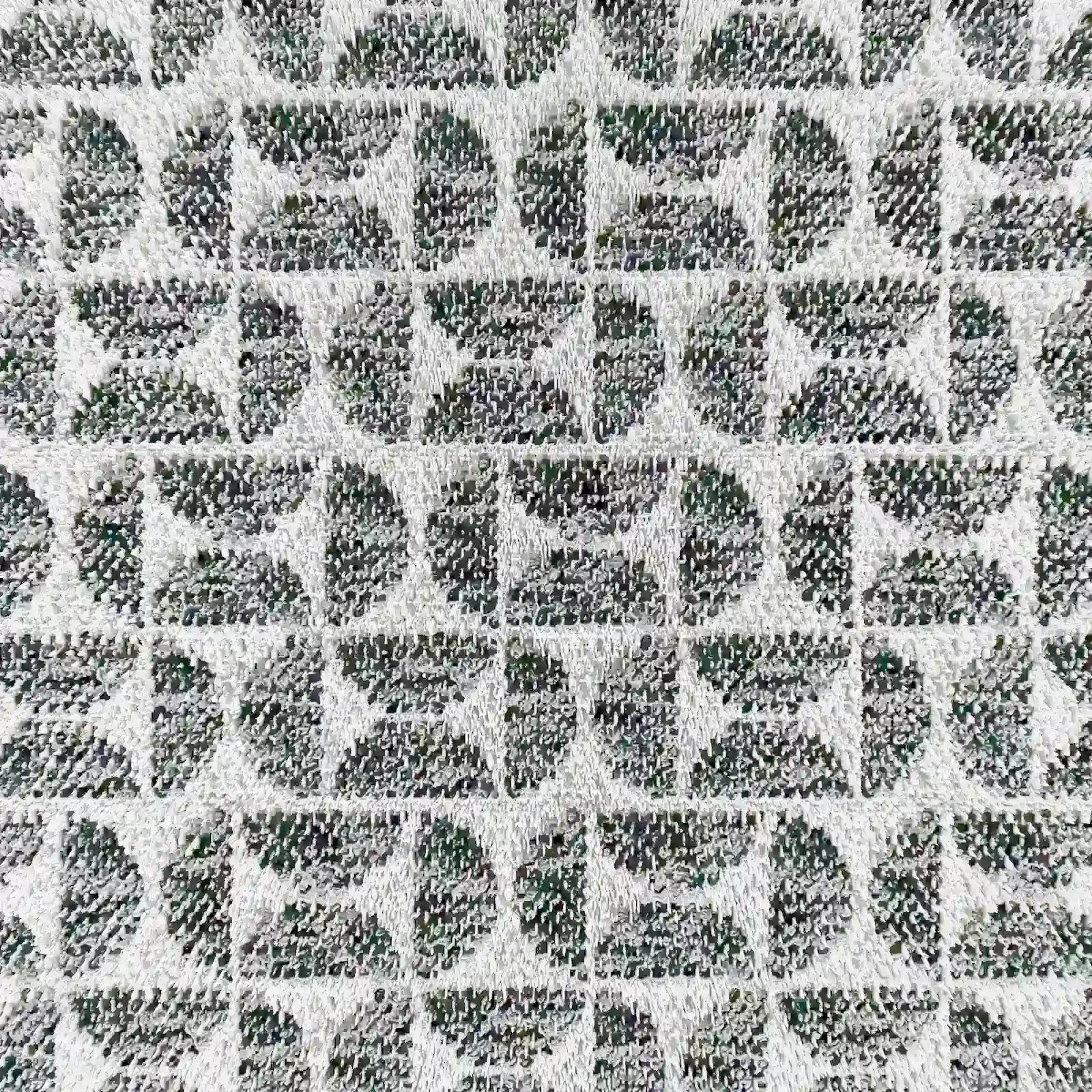 Un primo piano del modello Naxos Cuscino Decoro 45x45 in Lino di Divani.Store mostra un raffinato motivo geometrico nei toni del grigio e del nero, con quadrati, cerchi e linee: un tocco di eleganza per l'arredamento della tua casa.