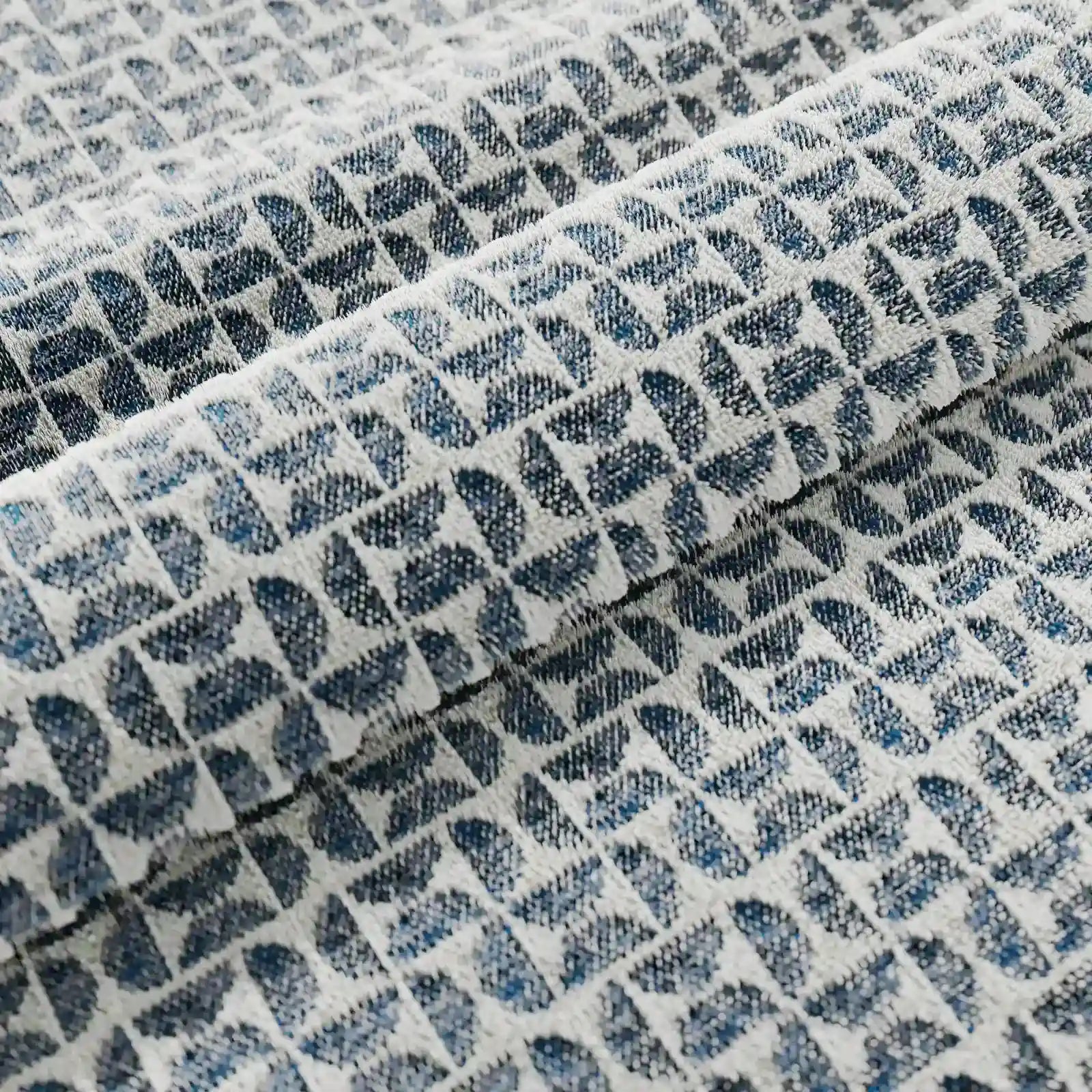 Primo piano sul tessuto piegato del cuscino decorativo Naxos 45x45 in lino di Divani.Store, caratterizzato da un motivo geometrico di triangoli blu scuro e azzurro su fondo bianco. La trama visibile esalta l'eleganza di questo cuscino decorativo.