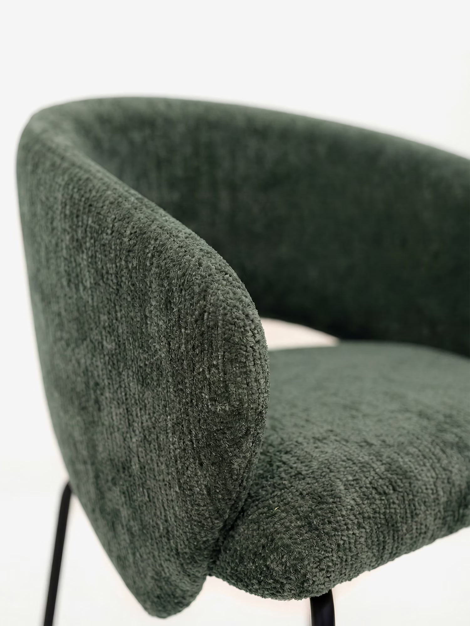 Primo piano della sedia imbottita Fosca di Divani.Store, caratterizzata da uno schienale arrotondato e braccioli in morbido tessuto certificato OEKO-TEX®, un elegante rivestimento verde e sottili gambe in metallo nero, il tutto su uno sfondo bianco a tinta unita.