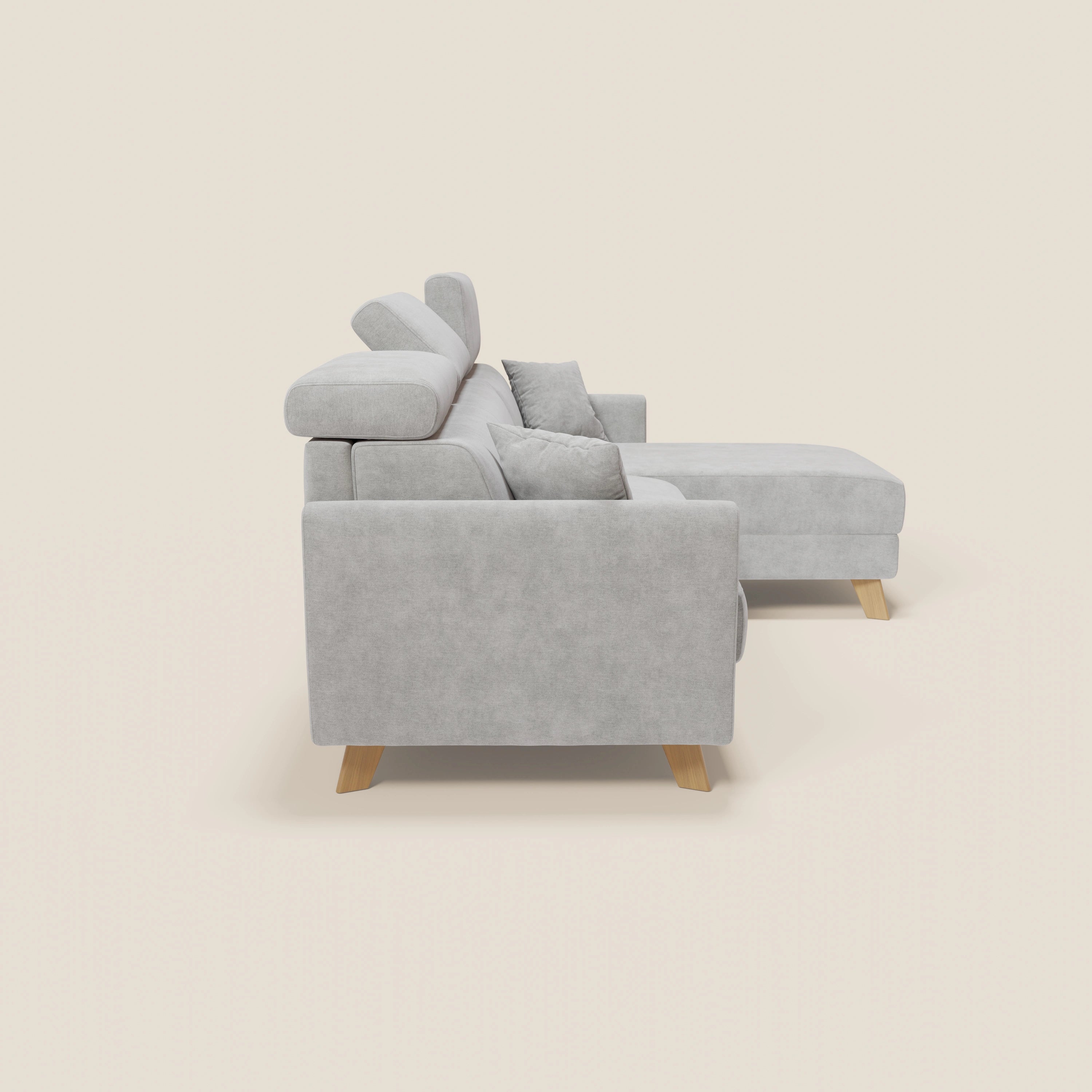 Vista laterale del divano letto angolare sfoderabile Francy di Divani.Store in T17 grigio, con chaise longue destra, poggiatesta reclinabili, gambe in legno chiaro, stile nordico e cuscini coordinati su sfondo bianco sporco.
