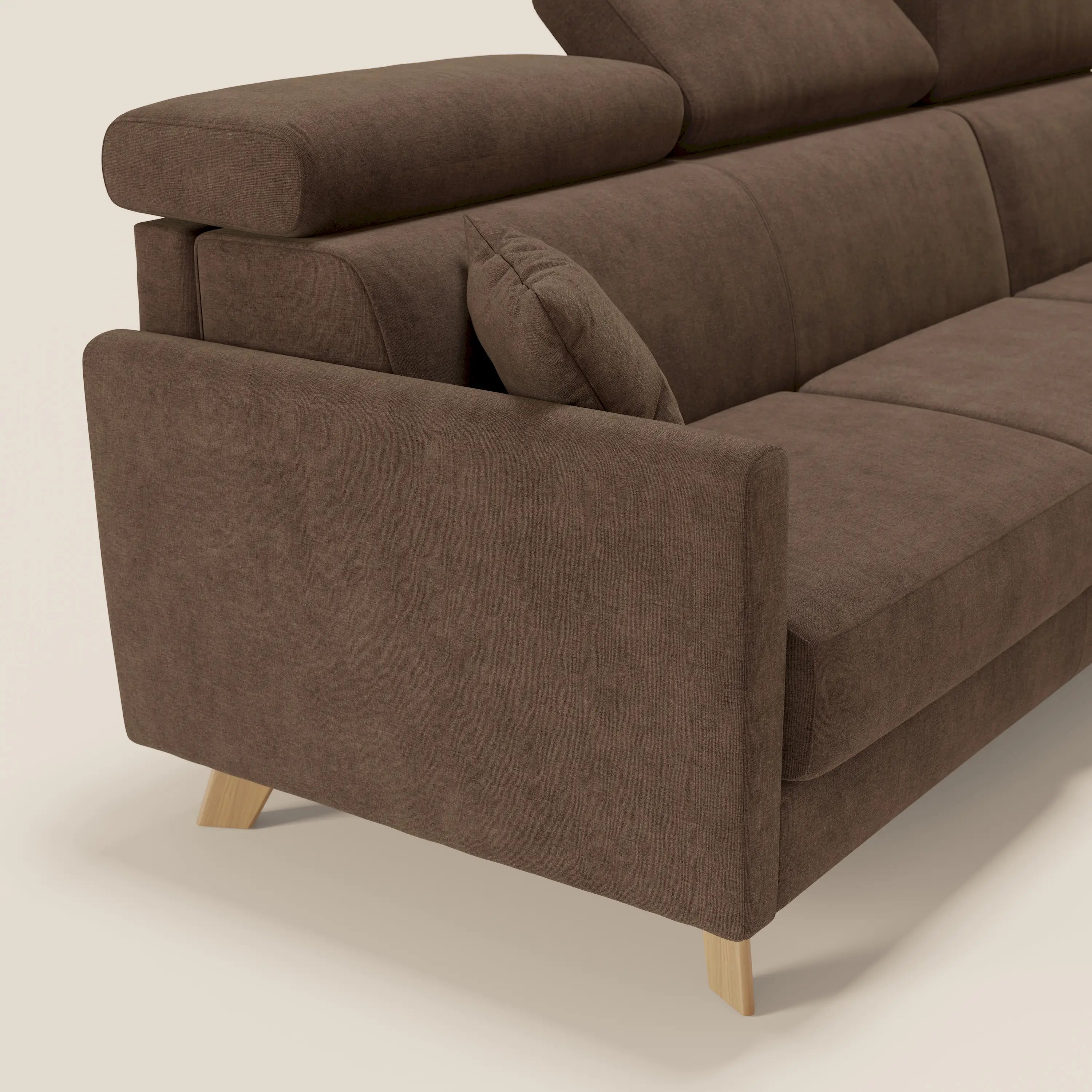 Primo piano del lato sinistro del divano letto angolare sfoderabile Francy di Divani.Store, in tessuto antimacchia marrone T17, con poggiatesta reclinabile, chaise longue contenitore, gambe in legno chiaro e cuscino in tinta su uno sfondo a tinta unita.