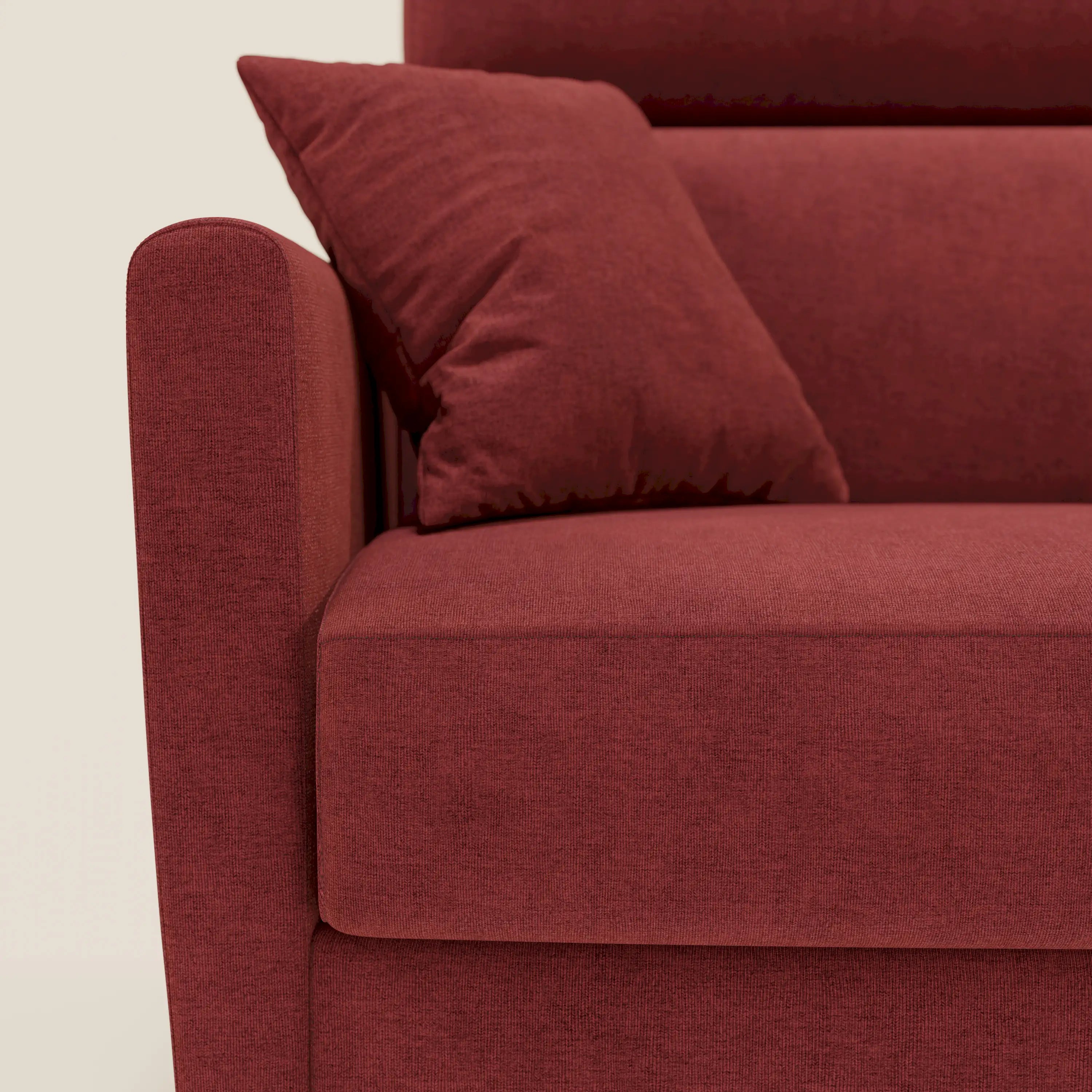 Primo piano del divano letto angolare sfoderabile Francy di Divani.Store in tessuto antimacchia T17 rosso, con bracciolo sinistro, cuscino di seduta e cuscino coordinato. Lo sfondo è in tinta unita beige chiaro. Include chaise longue e poggiatesta reclinabili.