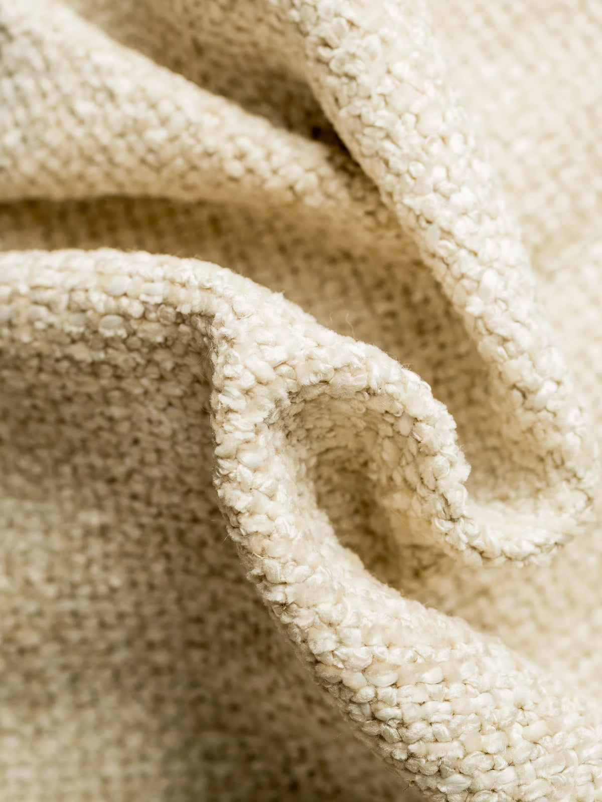 Primo piano del tessuto S01 LIVIGNO, un tessuto soft-touch materico misto lino, smacchiabile, di colore beige, dalla trama irregolare e a trama larga, drappeggiato in morbide pieghe per mettere in risalto la sua superficie irregolare e granulosa.