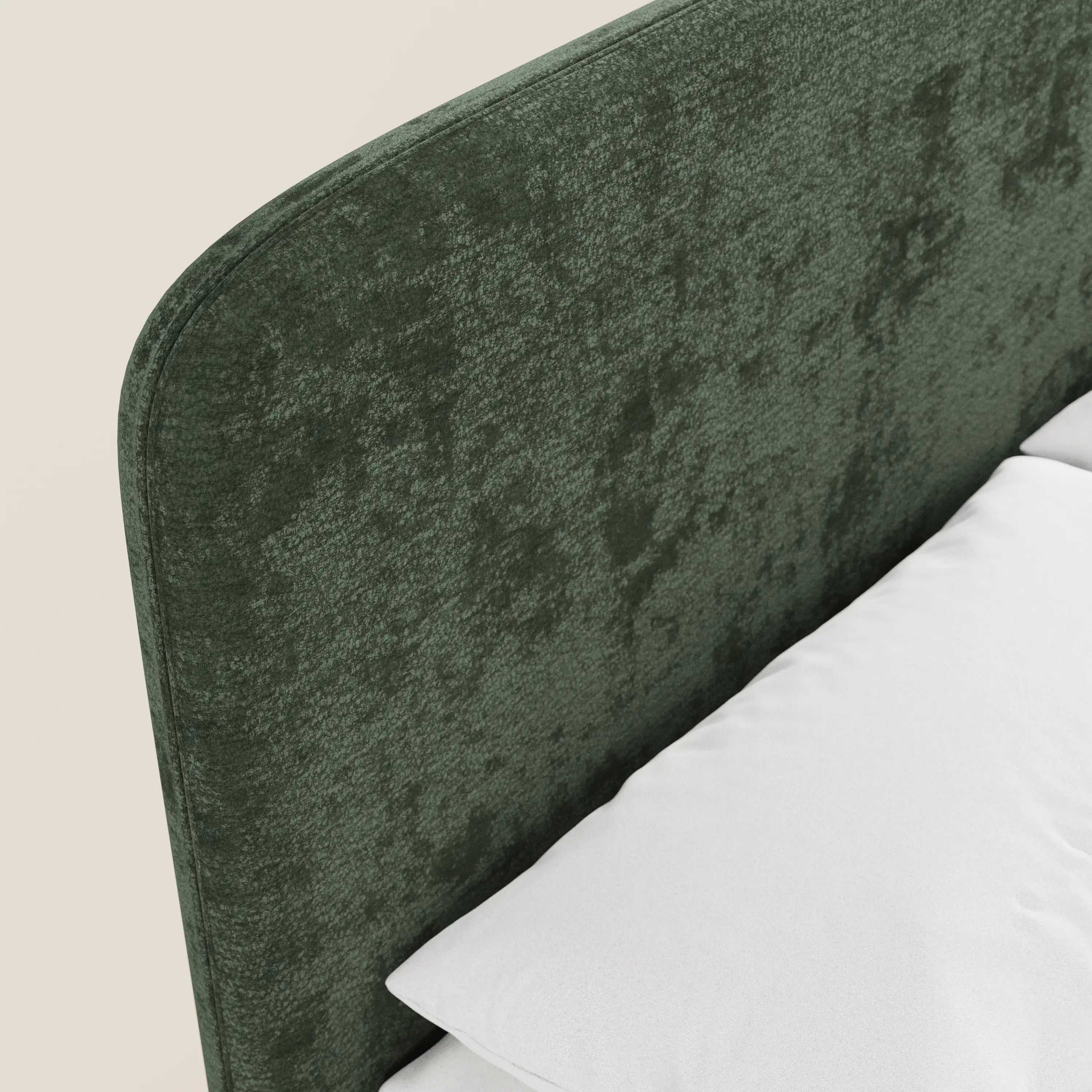 Primo piano del letto imbottito KAELOS Letto Minimal di Letti.store, caratterizzato da una testiera arrotondata in ciniglia verde scuro testurizzata. In basso a destra si intravedono un cuscino e un lenzuolo bianchi, che risaltano su uno sfondo chiaro e neutro.