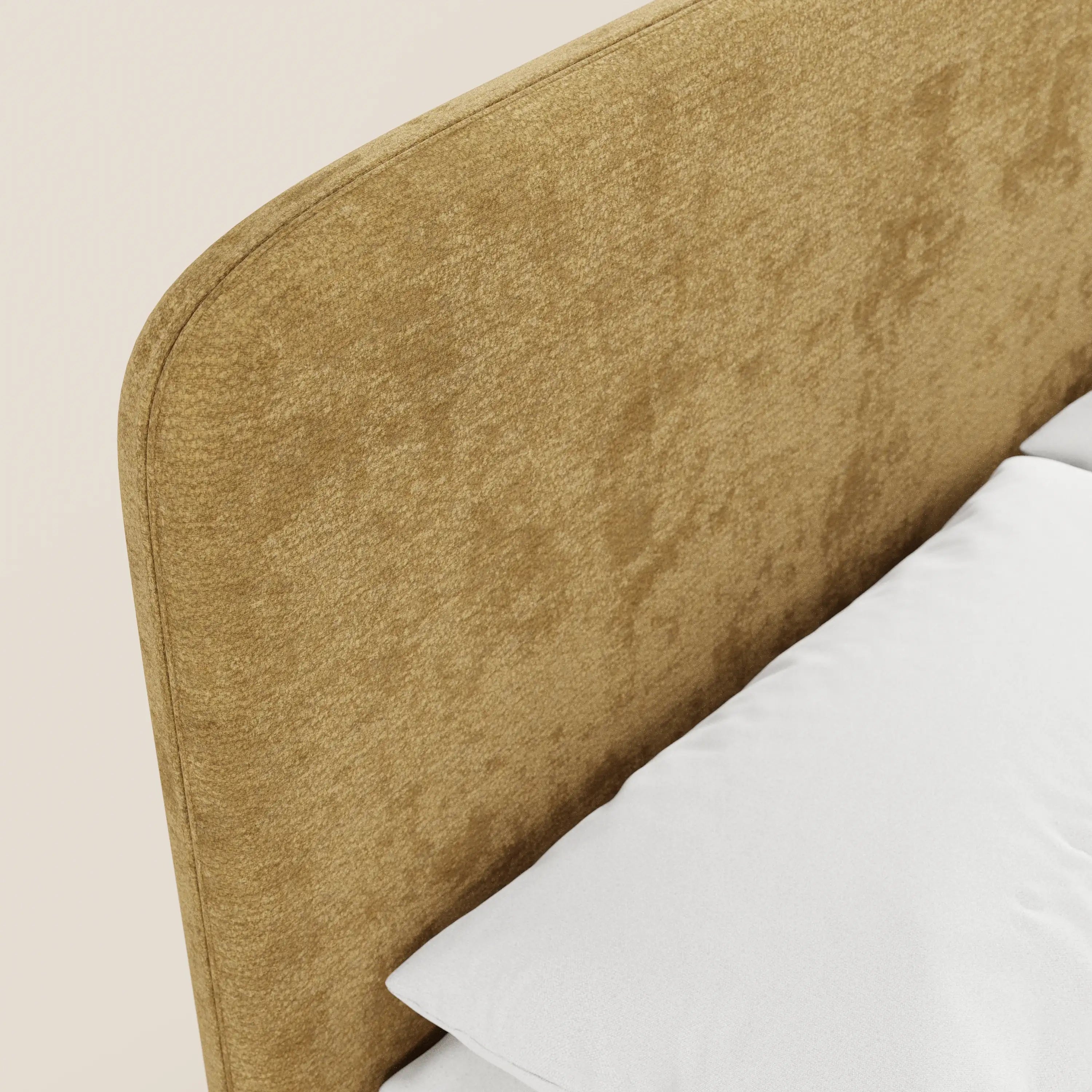 Primo piano del letto imbottito KAELOS minimal di Letti.store, caratterizzato da una morbida testiera arrotondata rivestita in ciniglia giallo senape. Su uno sfondo beige chiaro si intravedono un cuscino bianco e la biancheria da letto.