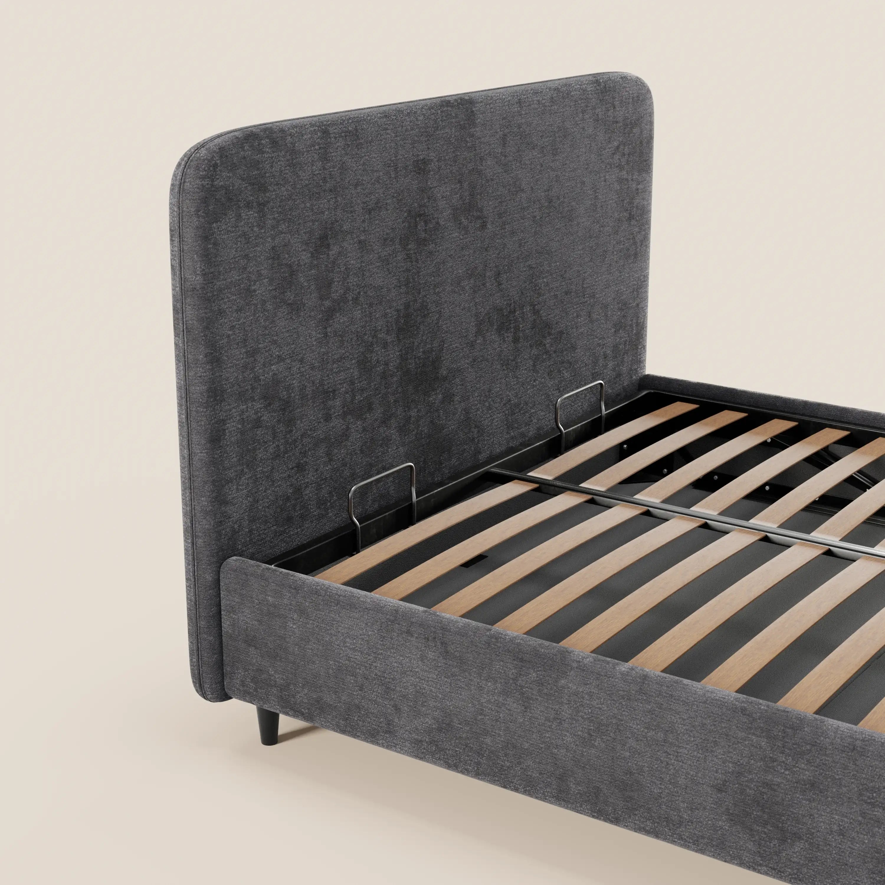 Il letto KAELOS minimal imbottito di Letti.store è un letto moderno caratterizzato da una testiera alta e ricurva in tessuto ciniglia, gambe alte, vano contenitore e doghe in legno. Nella foto è raffigurato in grigio scuro su uno sfondo beige chiaro.