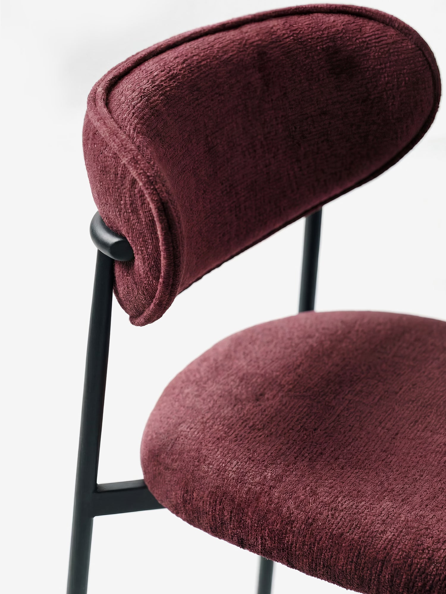 Primo piano della sedia Luce, imbottita in morbida ciniglia bordeaux con schienale curvo e struttura in metallo nero opaco di Divani.Store: questo design moderno risalta sullo sfondo bianco.