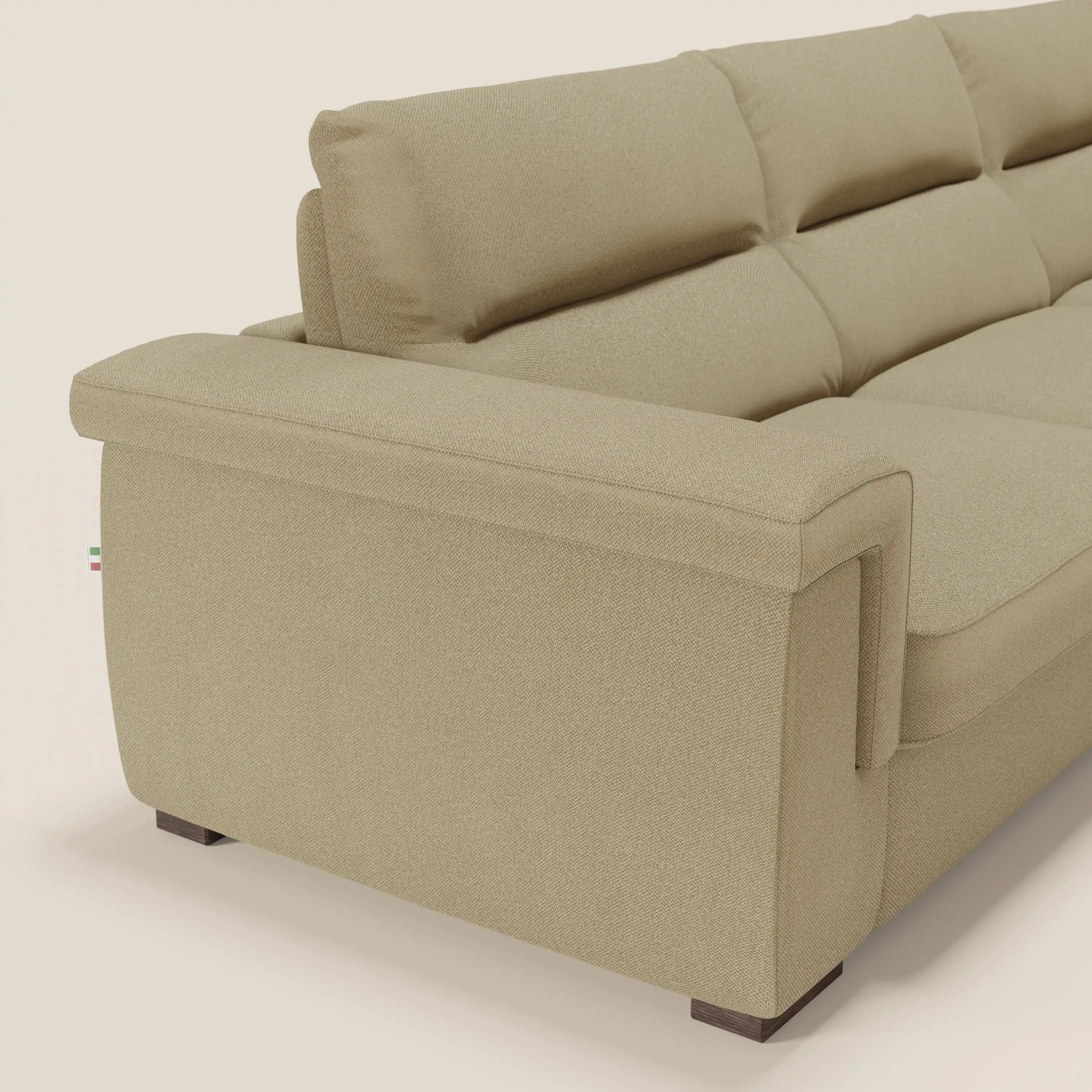 Un primo piano del divano letto angolare Magnolia con Penisola Contenitore di Divani.Store in tessuto smacchiabile T05 cammello mostra il bracciolo sinistro, gli schienali imbottiti, le linee pulite, le gambe squadrate scure e lo stile minimalista su uno sfondo bianco sporco.