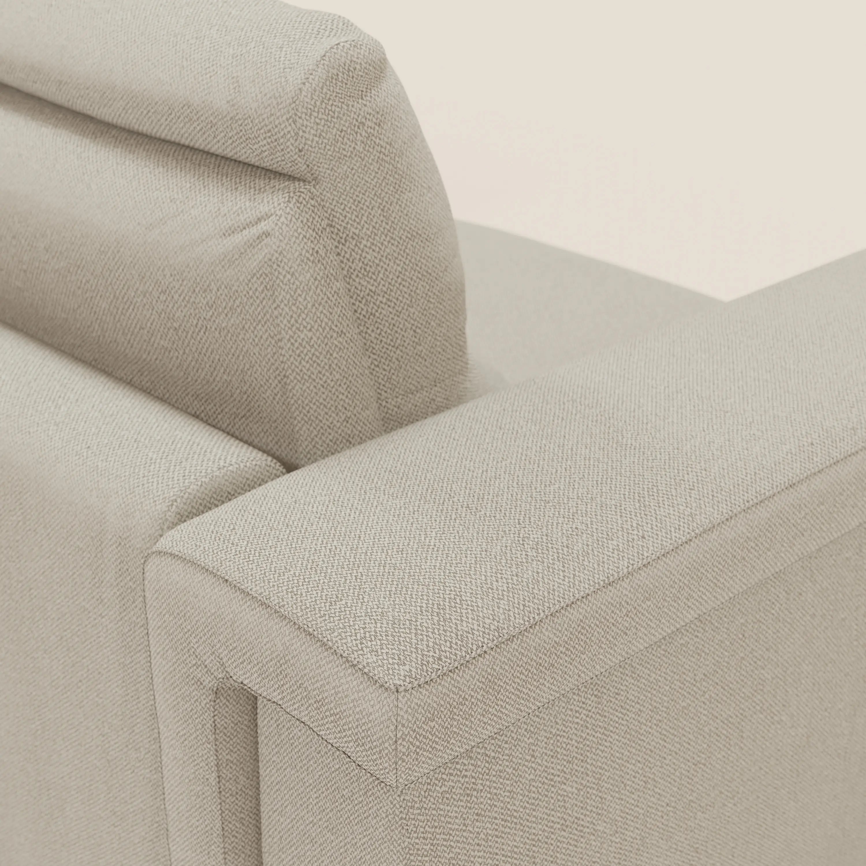 Primo piano del divano letto angolare Magnolia con Penisola Contenitore di Divani.Store in tessuto smacchiabile T05 panna, che mostra il rivestimento strutturato, le linee pulite dei cuscini dei braccioli e dello schienale e la poltrona integrata. Lo sfondo è un semplice bianco sporco.