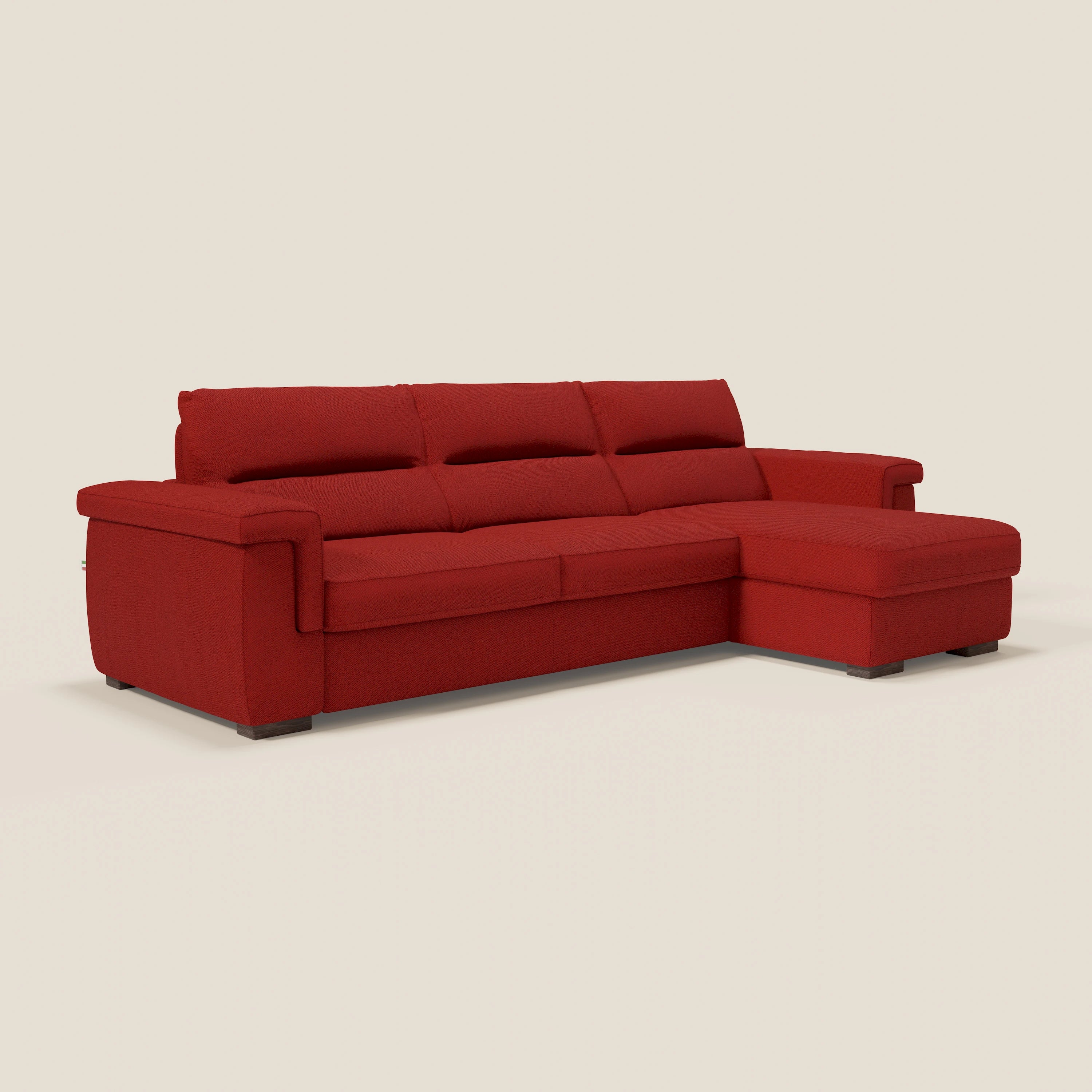 Un moderno divano letto angolare Magnolia con penisola contenitore di Divani.Store in tessuto antimacchia T05 rosso con cuscini di seduta rigidi, ampi braccioli e chaise lounge destra su basse gambe quadrate in legno, su sfondo beige.