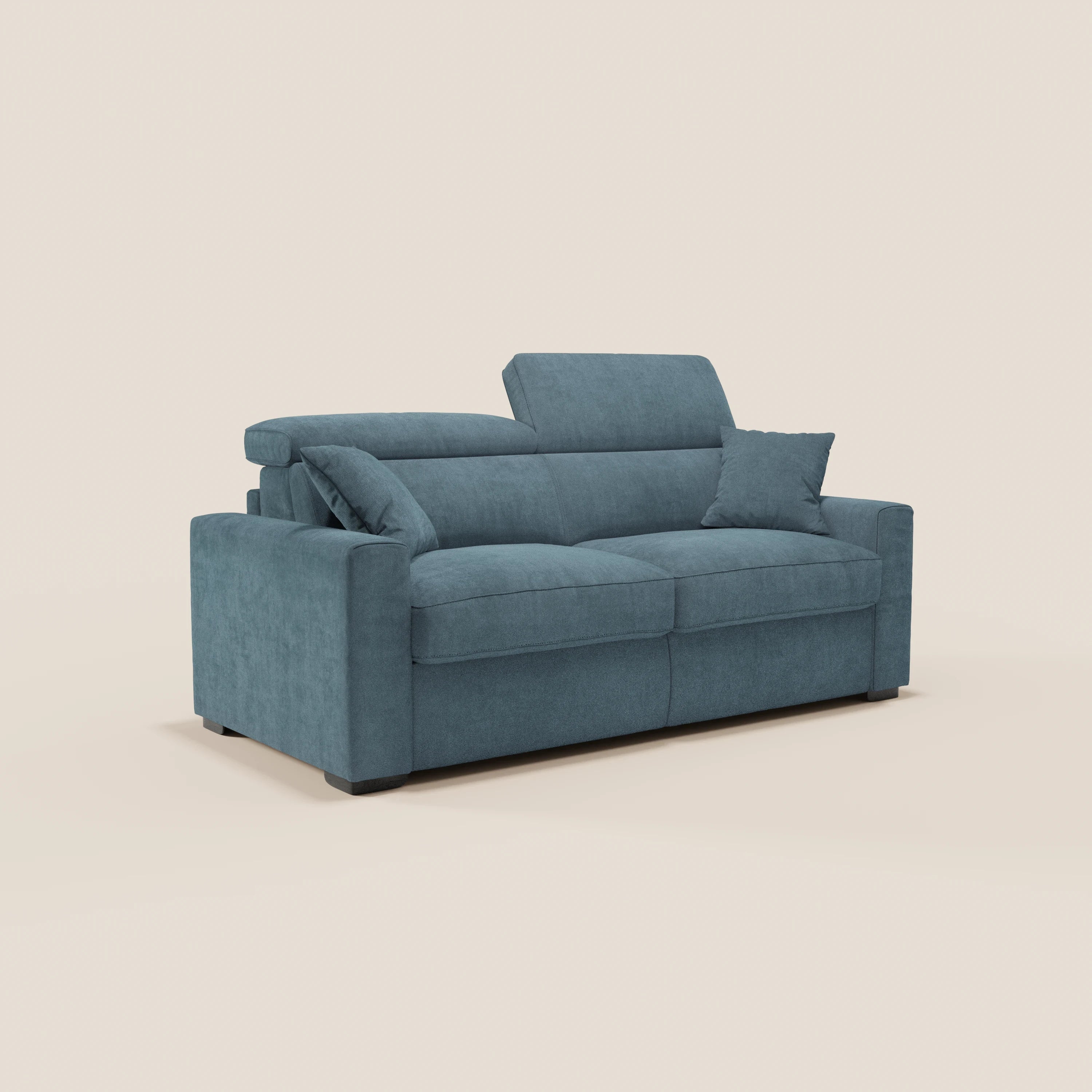 Il divano letto a 3 posti Maximus di Divani.Store è dotato di un materasso alto 20 cm, poggiatesta reclinabile, due cuscini di seduta, ampi braccioli e tessuto lavabile certificato Oeko-Tex in blu, raffigurato con un cuscino decorativo abbinato su uno sfondo bianco sporco.